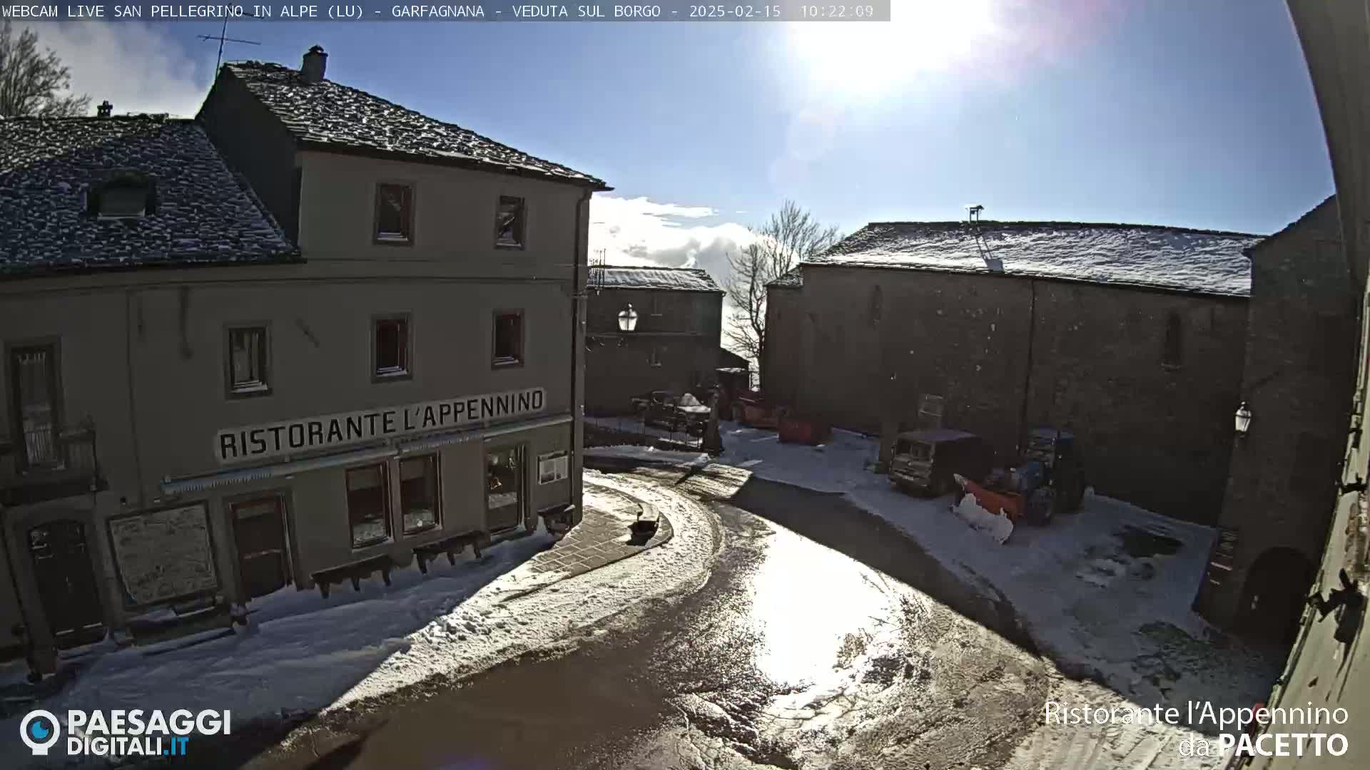 A sunny, snow-dusted village square with several buildings, including a restaurant, and some vehicles.