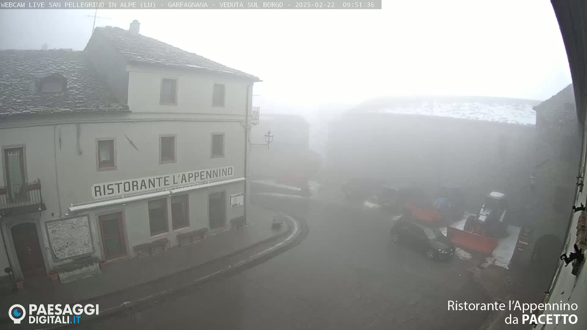 A foggy view of a town square, featuring a building with a restaurant called "Ristorante l'Appennino," and a few vehicles are barely visible in the mist.