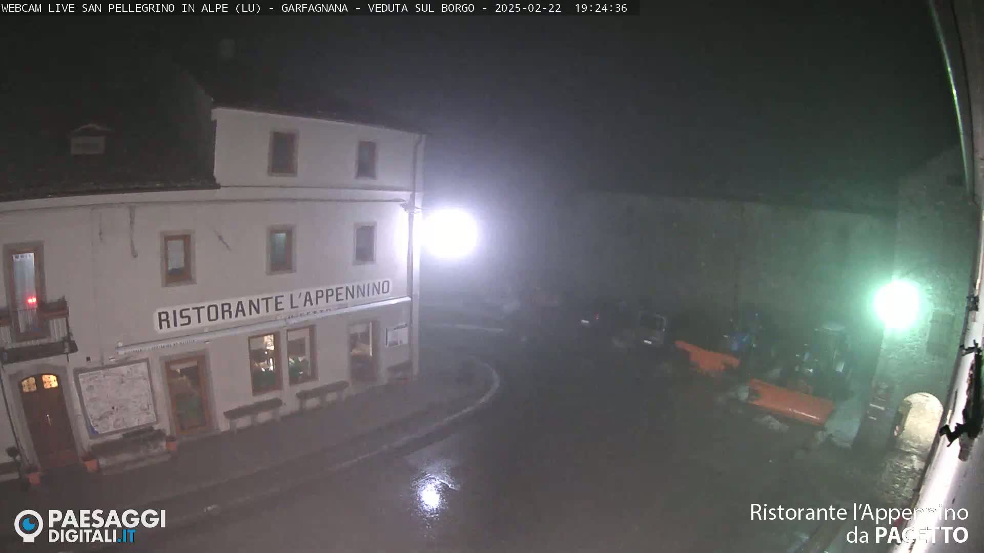 A nighttime view of a restaurant called Ristorante L'Appennino, showing a wet street and parked vehicles under dim lighting during rain.