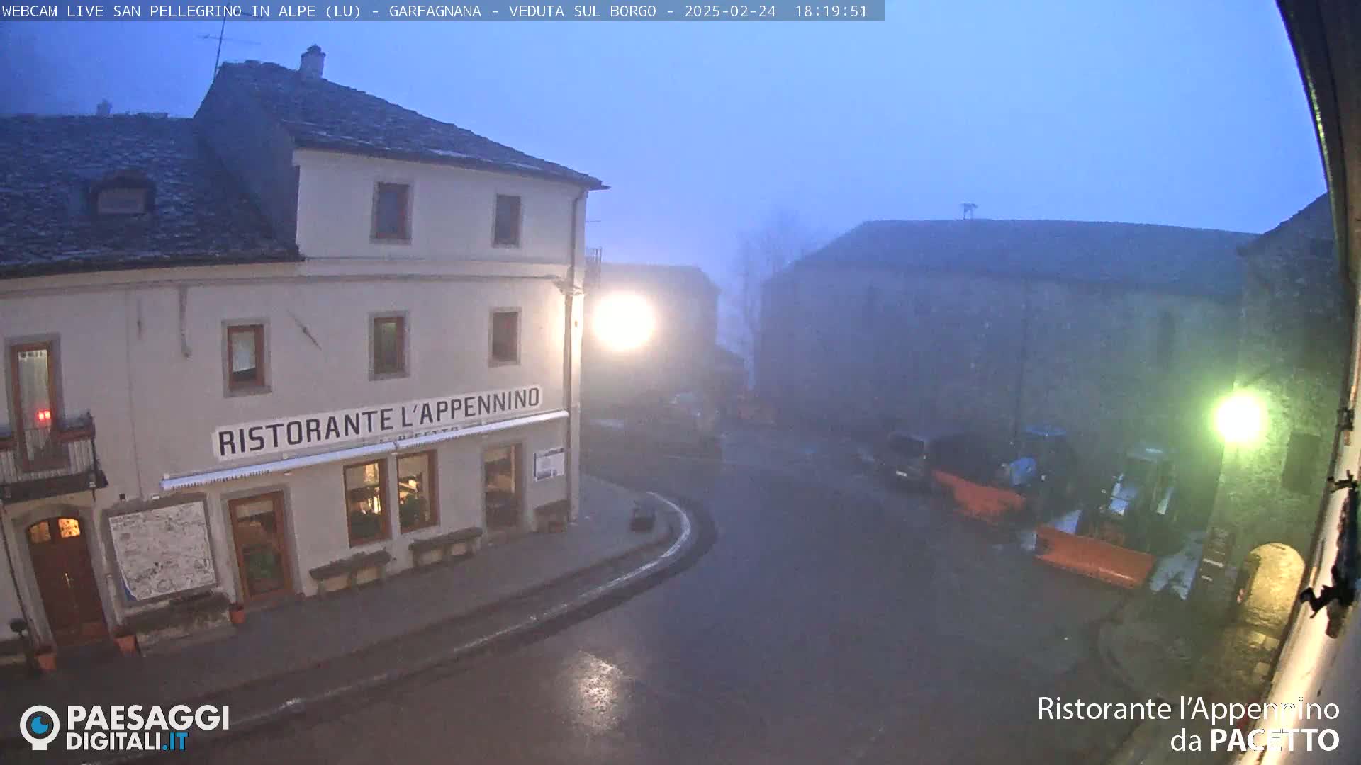 A foggy, dimly lit town square at night, featuring a restaurant called "Ristorante l'Appennino" and several other buildings.