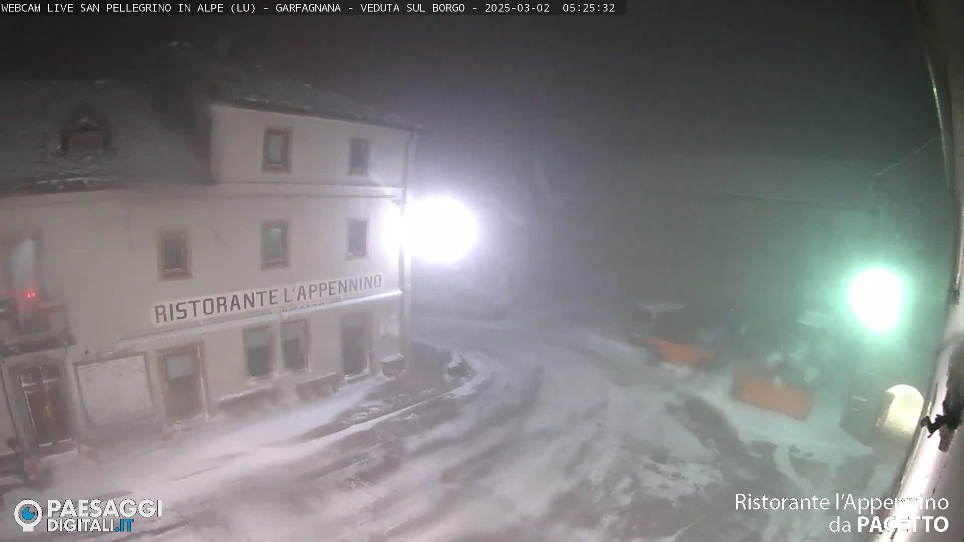 A snow-covered street at night, illuminated by a streetlight, shows a restaurant called "Ristorante l'Appennino" with vehicles parked nearby.
