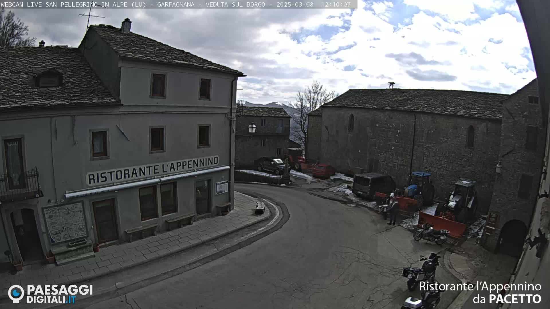 A partly cloudy day reveals a town square with stone buildings, vehicles, and construction equipment; a restaurant is visible.