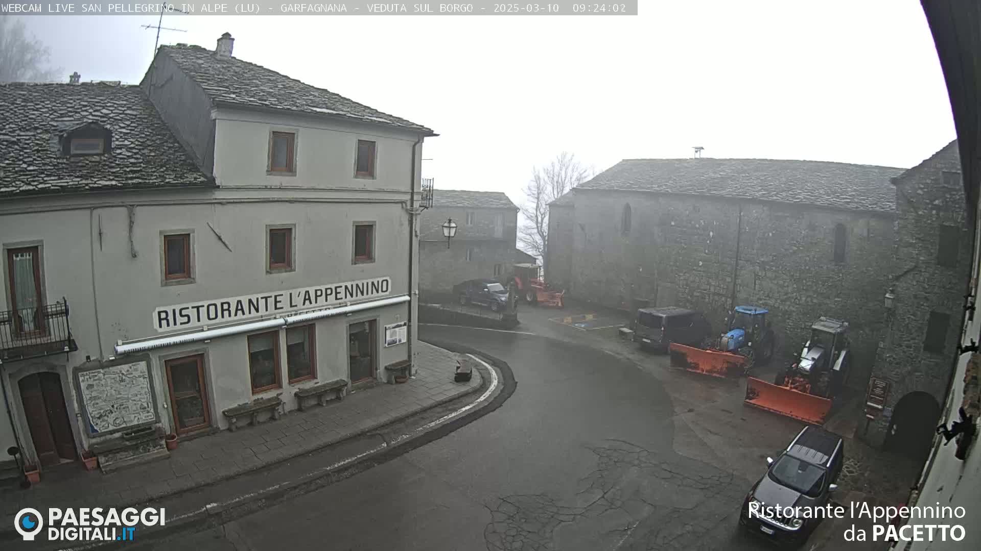 A foggy town square with several buildings, vehicles, and snowplows is visible.