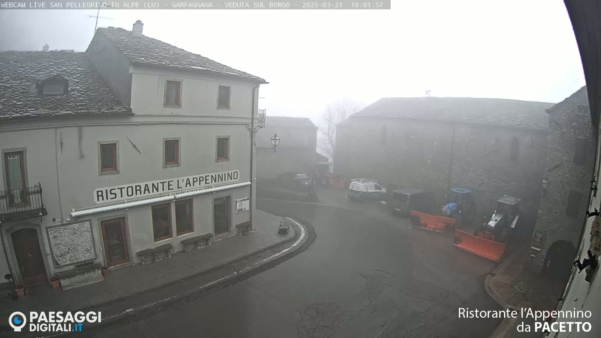 A foggy town square with a restaurant, several buildings, and snowplows.