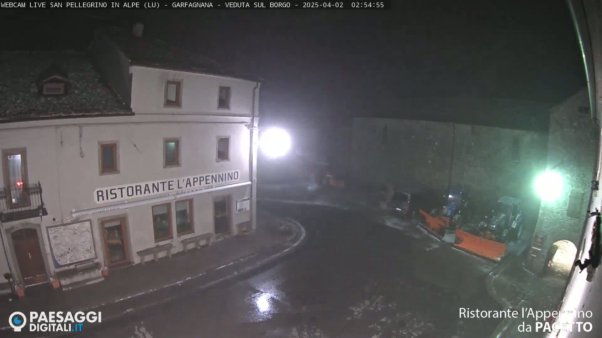 A nighttime, snowy scene shows a restaurant called Ristorante L'Appennino, a snowplow, and several parked cars in a small town square.