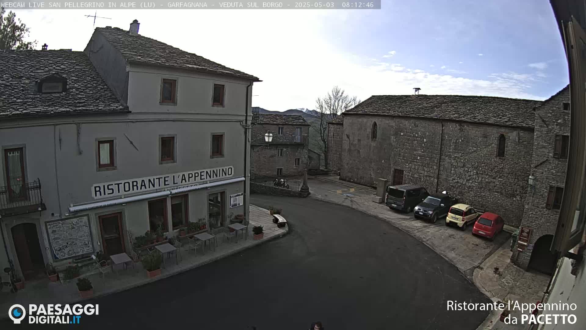 A quaint village square with several parked cars, under a mostly clear sky, features a stone building and a restaurant called "Ristorante L'Appennino".