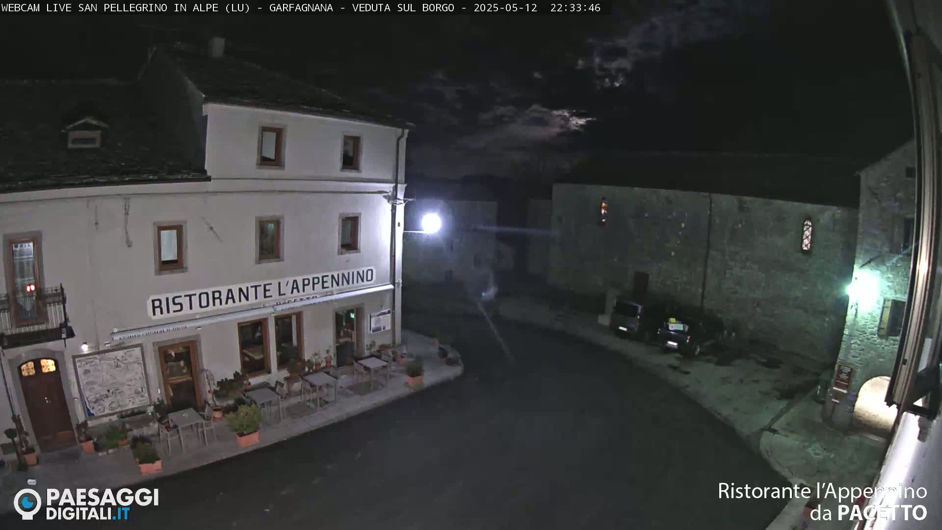 A nighttime view of a restaurant called "Ristorante L'Appennino" in a quiet village square, under a partly cloudy sky.