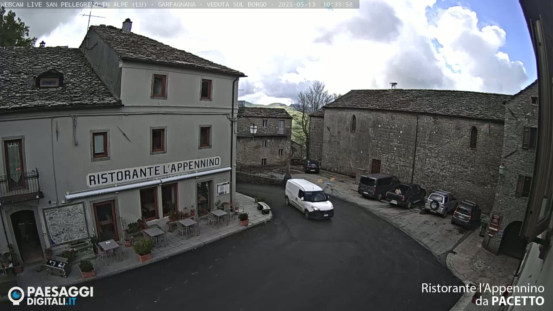 A partly cloudy day reveals a quaint European village square with several parked cars, a white van, and a restaurant called "Ristorante L'Appennino."