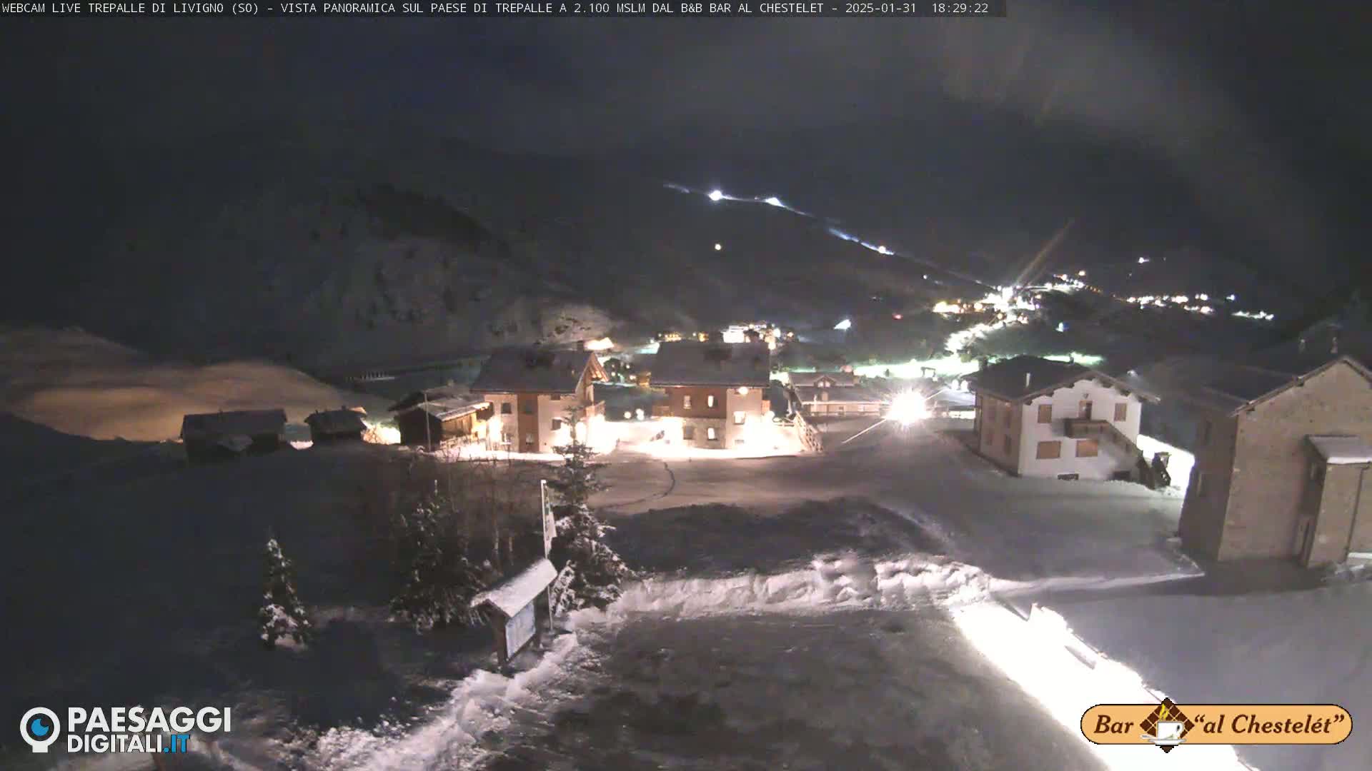 A snow-covered village at night, illuminated by building lights, is nestled in a mountainous area.