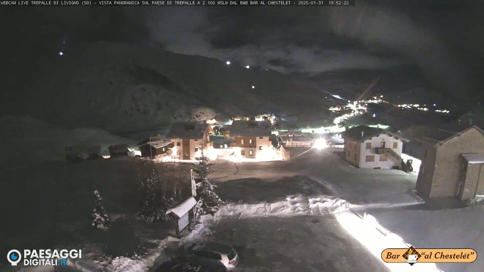 A snow-covered village at night is illuminated under a cloudy sky.