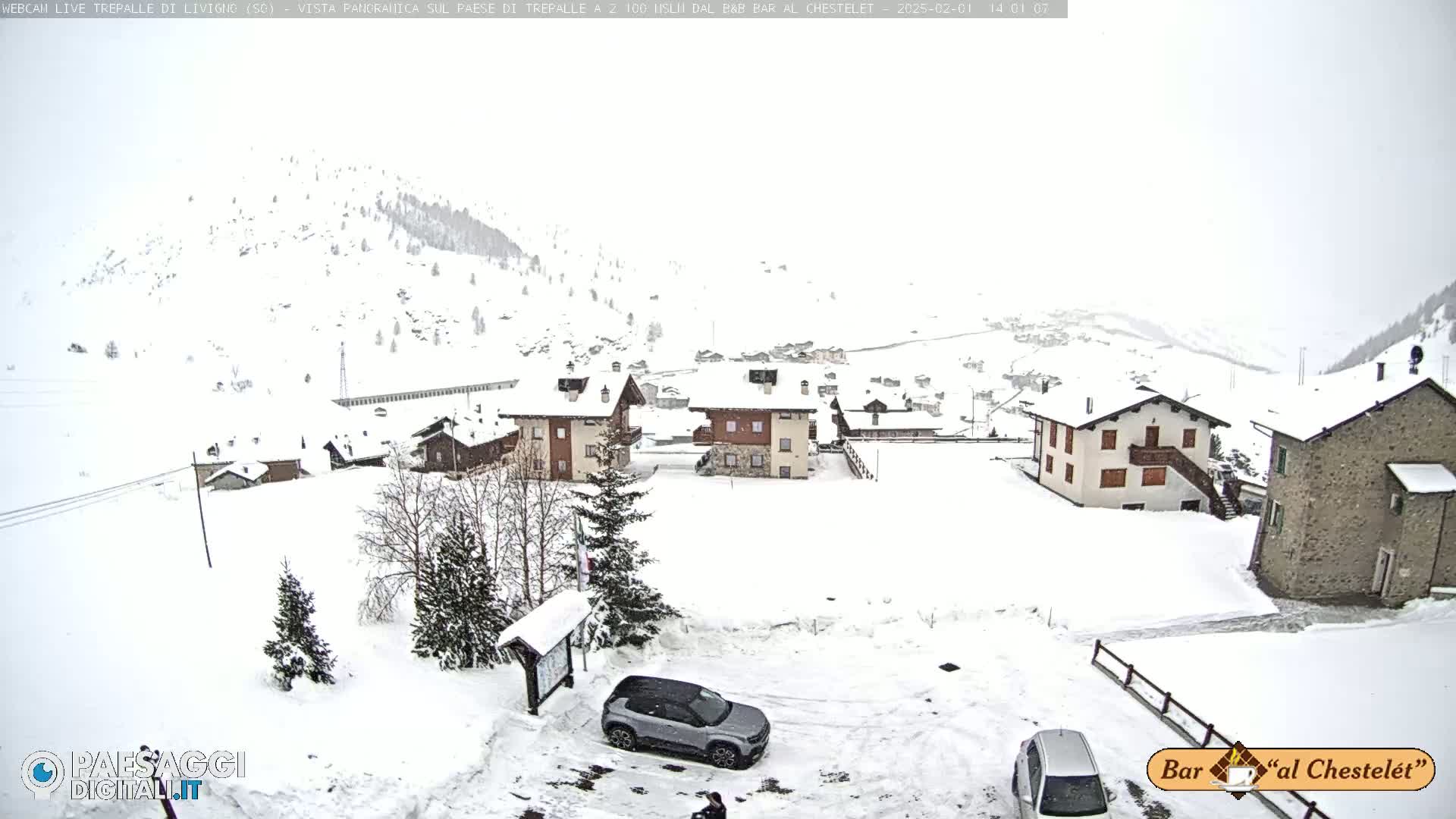 A snow-covered village in a mountainous region is lightly dusted with falling snow.