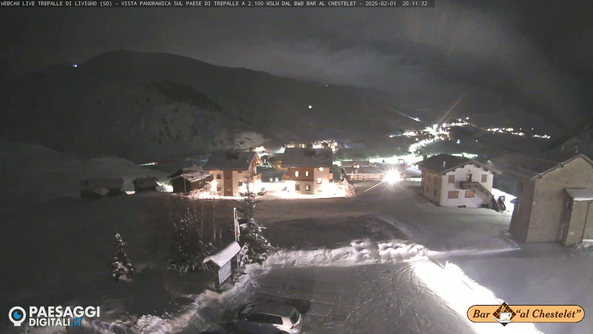 A snow-covered village at night, nestled in a valley under a cloudy sky.