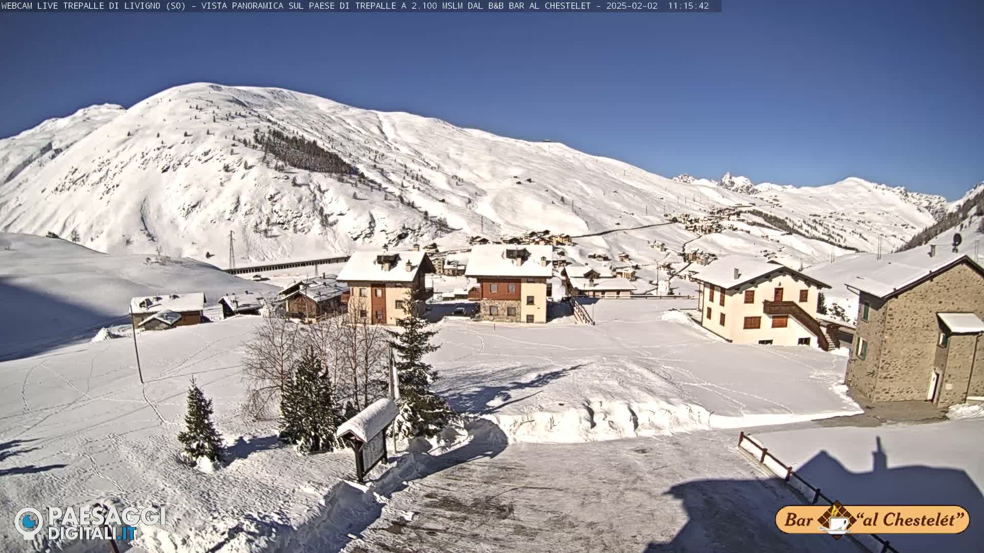 A snow-covered village nestled in a valley surrounded by snow-dusted mountains under a clear, sunny sky.