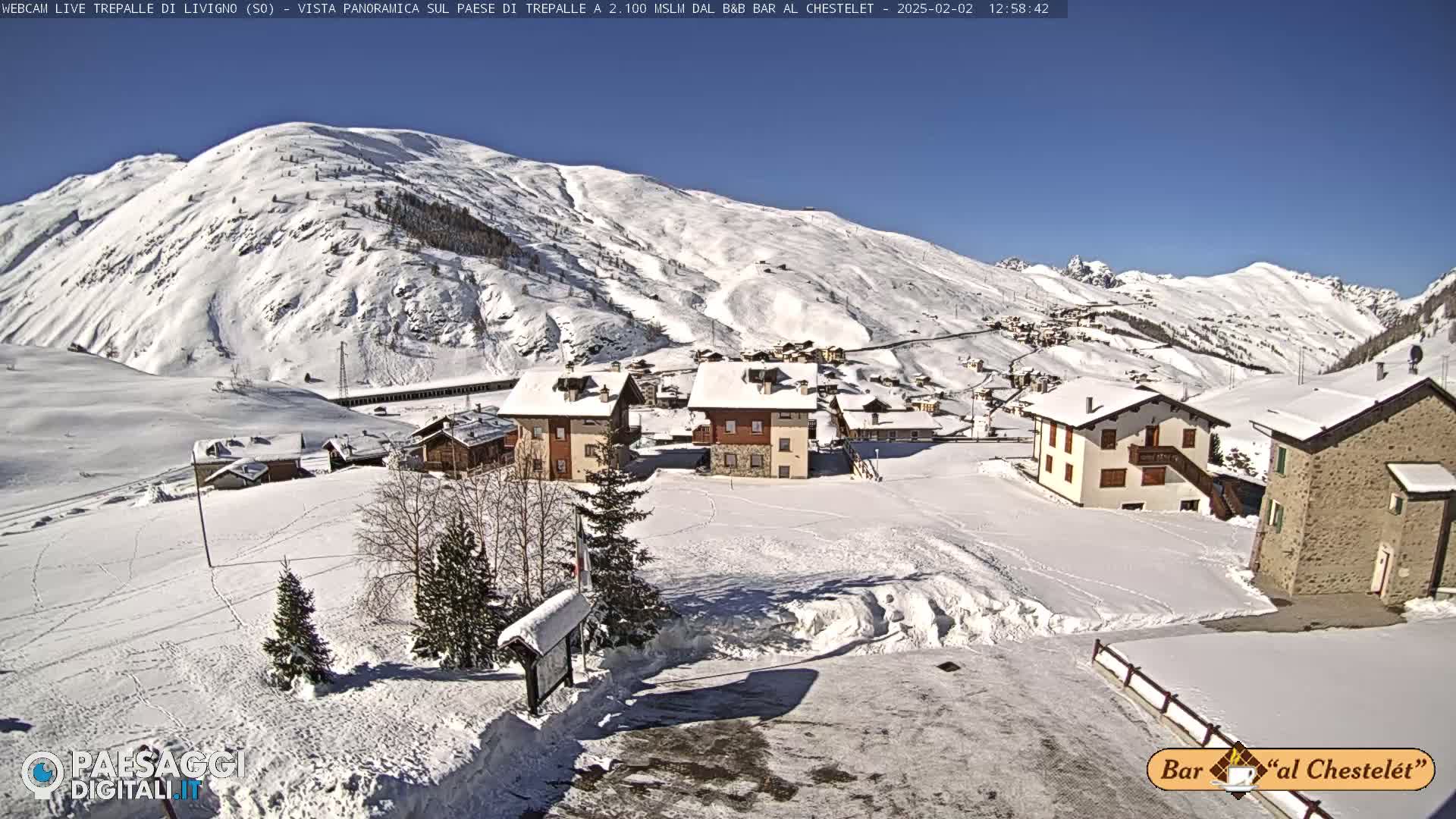 A snow-covered village nestled in a valley surrounded by snow-capped mountains under a clear blue sky.