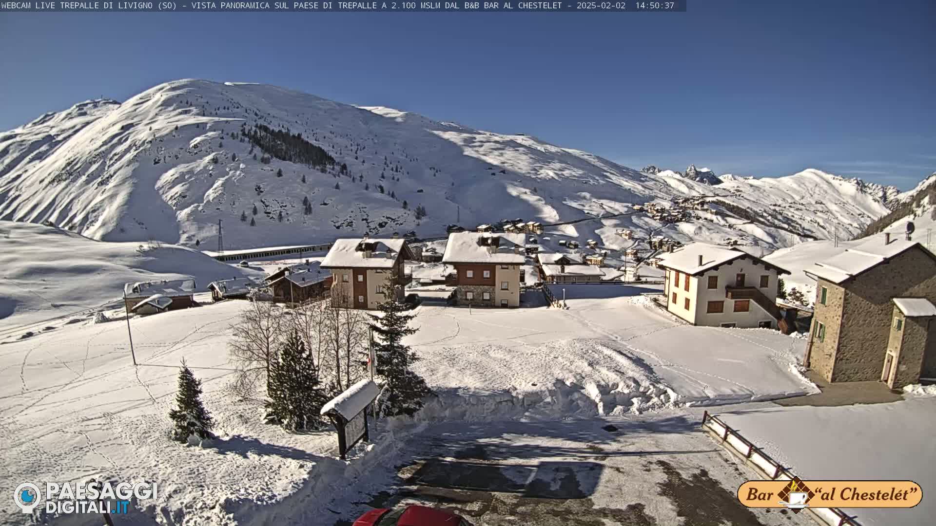 A snow-covered village nestled in a valley surrounded by snow-capped mountains under a clear blue sky.