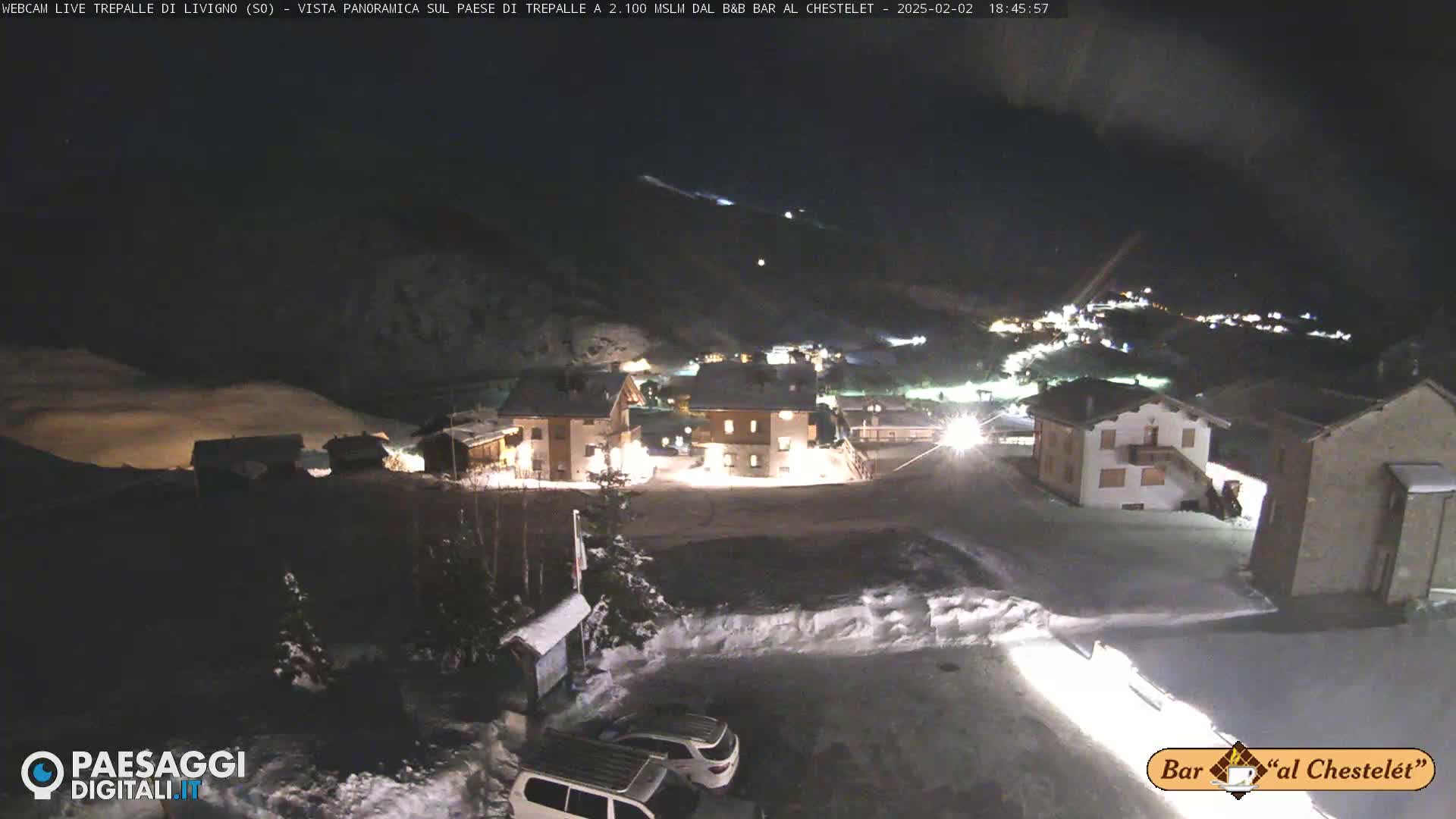 A nighttime, snowy panorama of a small village illuminated with lights, under a dark sky.