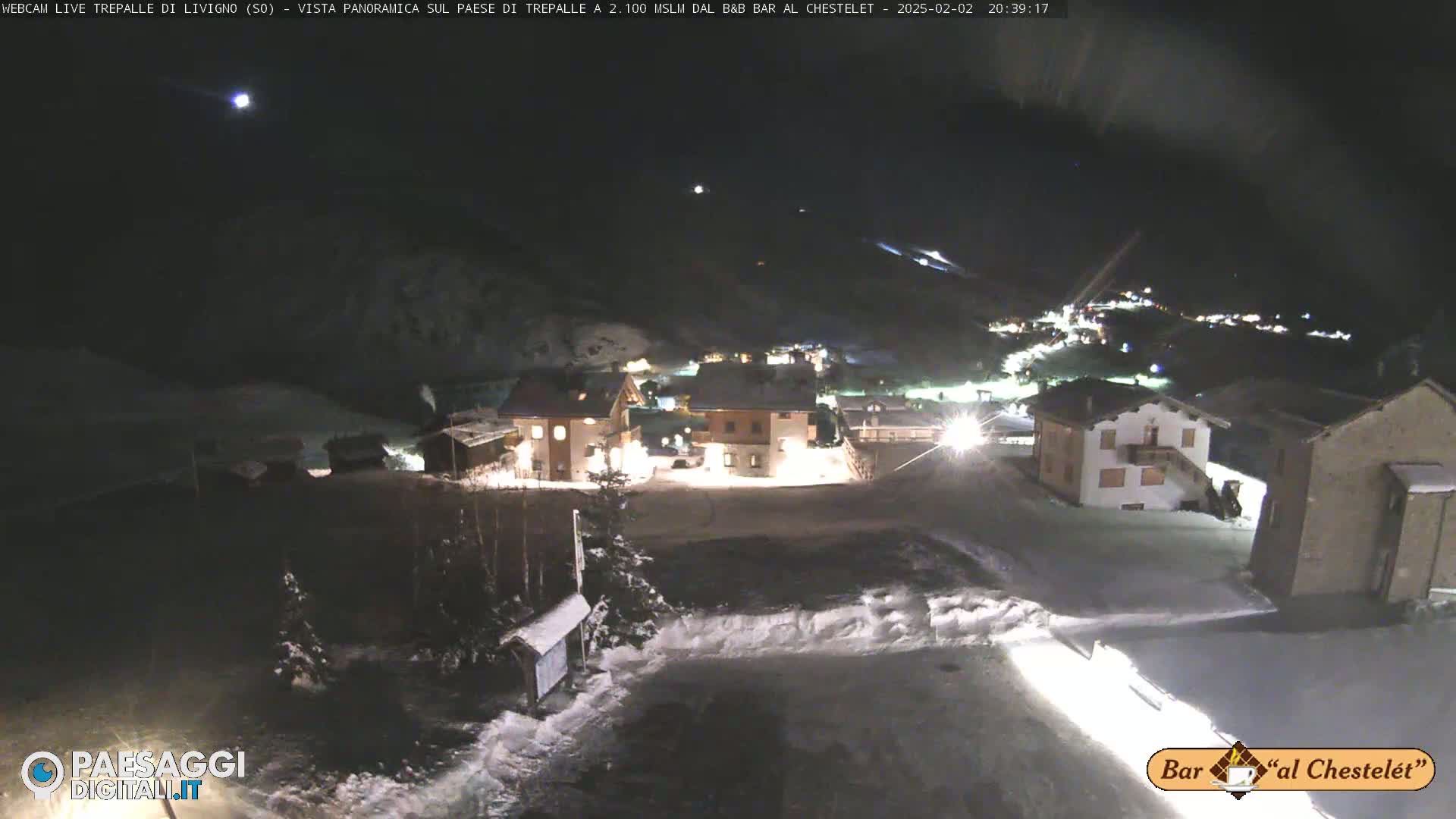 A snow-covered village is illuminated at night under a dark sky with a bright moon.