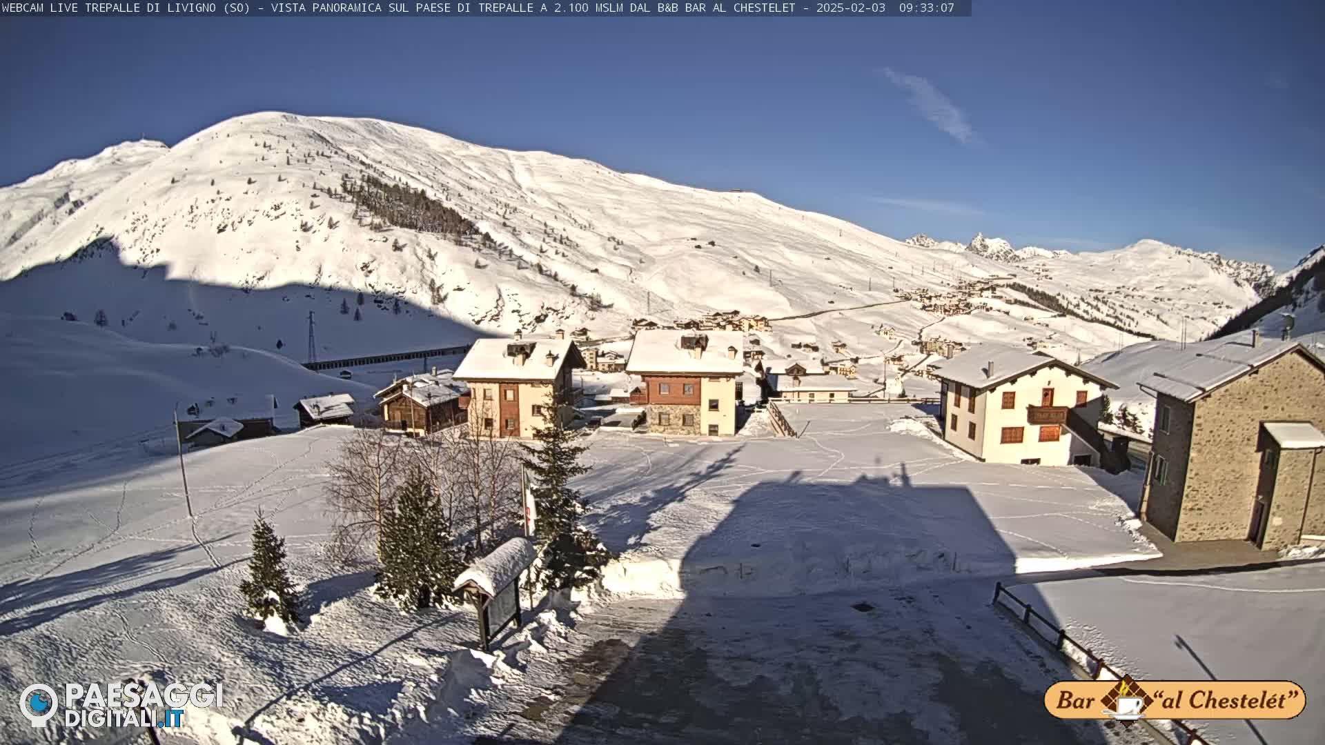A snow-covered village nestled in a valley between snow-covered mountains on a sunny day.