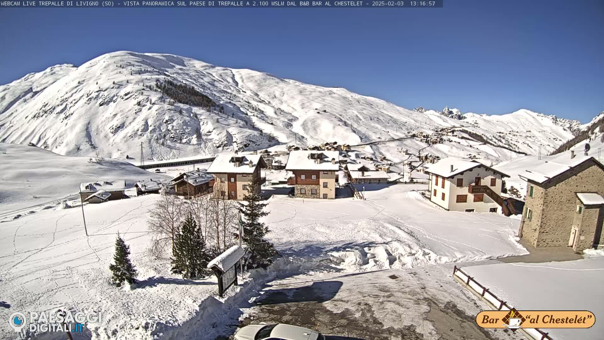 A snow-covered village nestled in a valley surrounded by snow-dusted mountains under a clear blue sky.