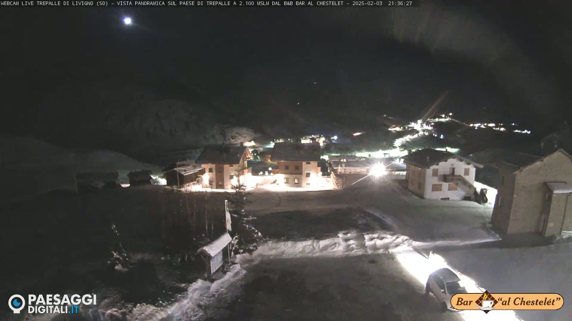 A nighttime, snowy scene shows a small village illuminated under a clear, dark sky.