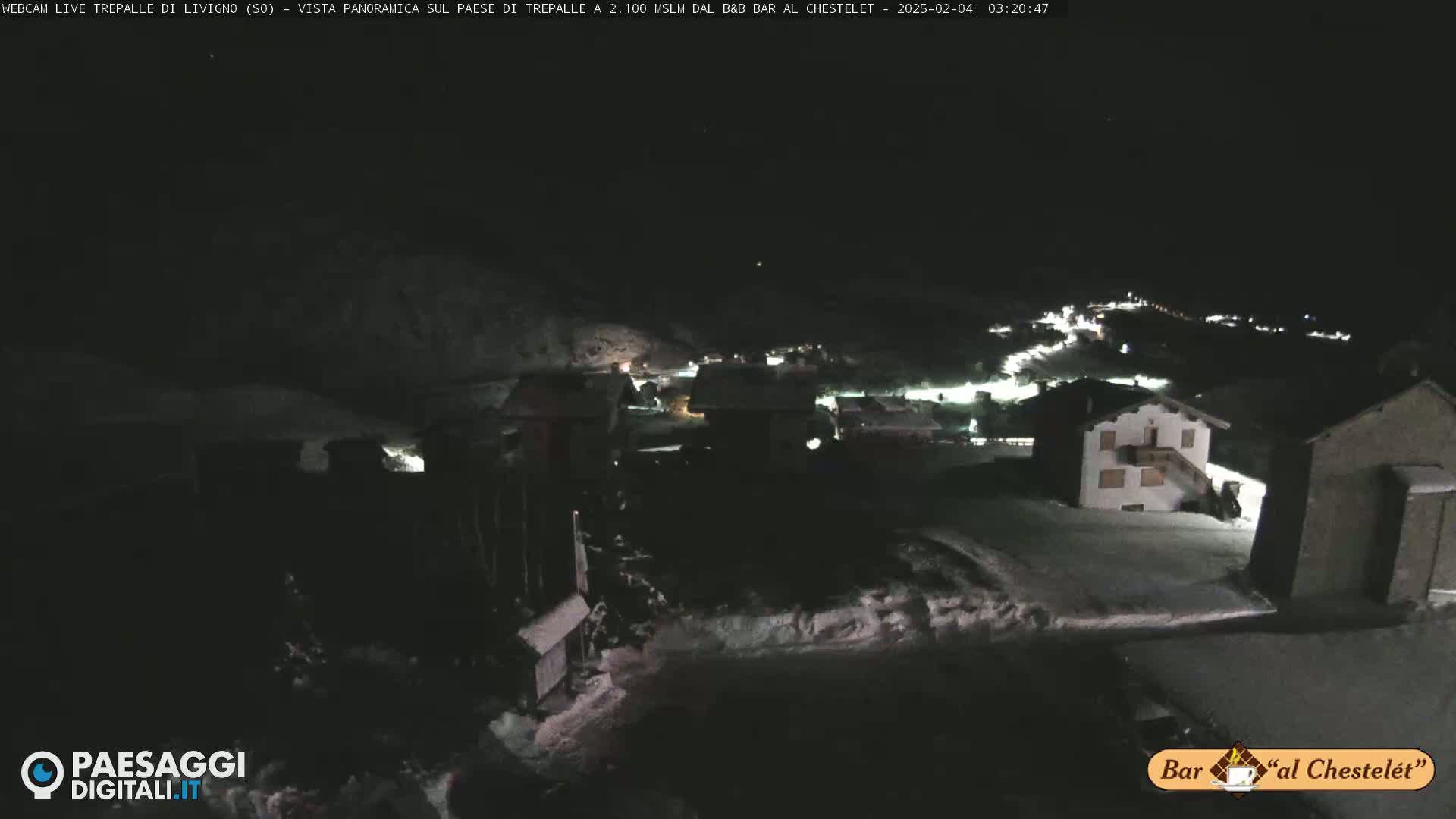 A nighttime, snow-covered village is illuminated by scattered lights under a dark sky.