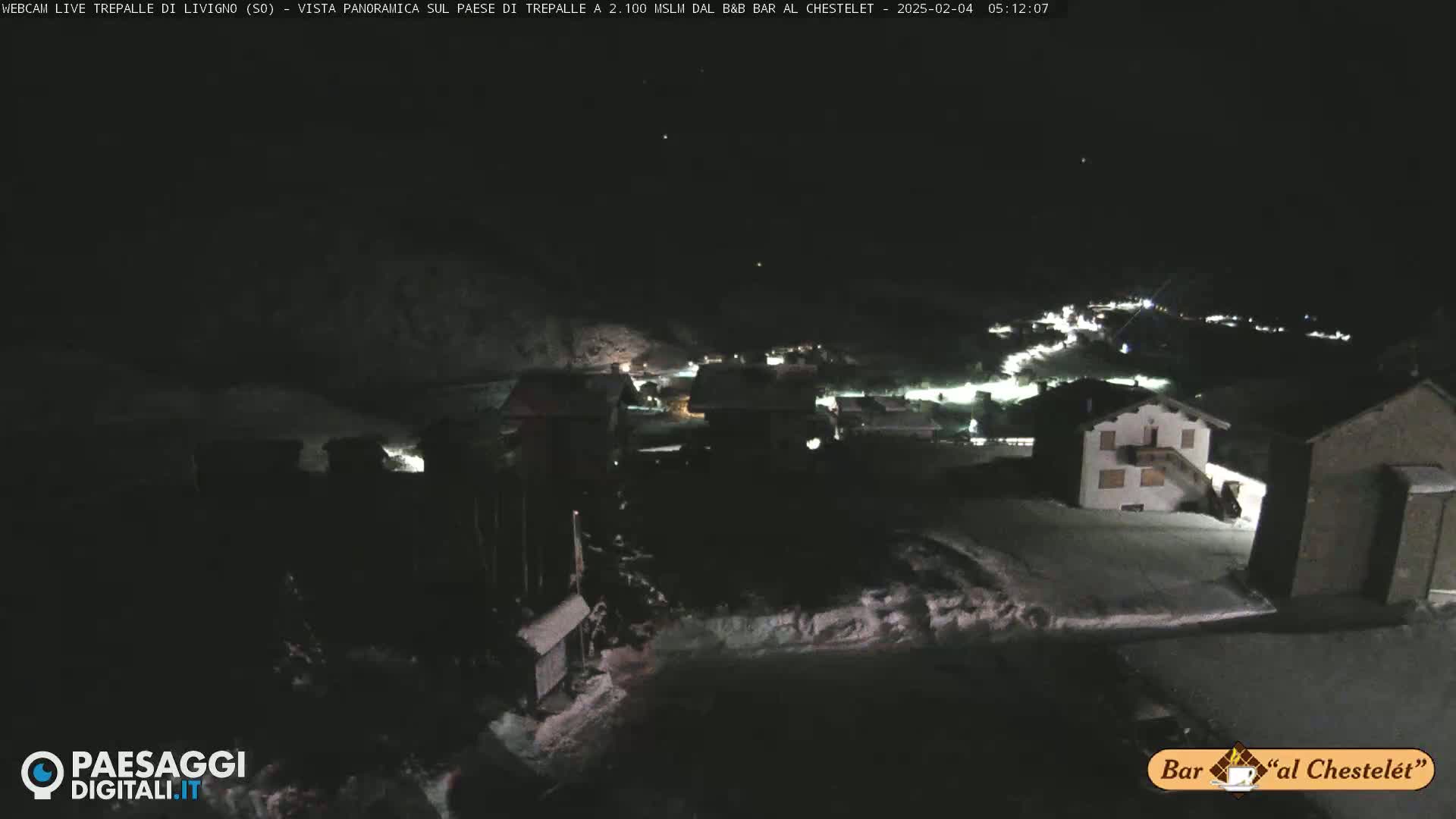 A snow-covered village at night is illuminated by scattered lights under a dark sky.