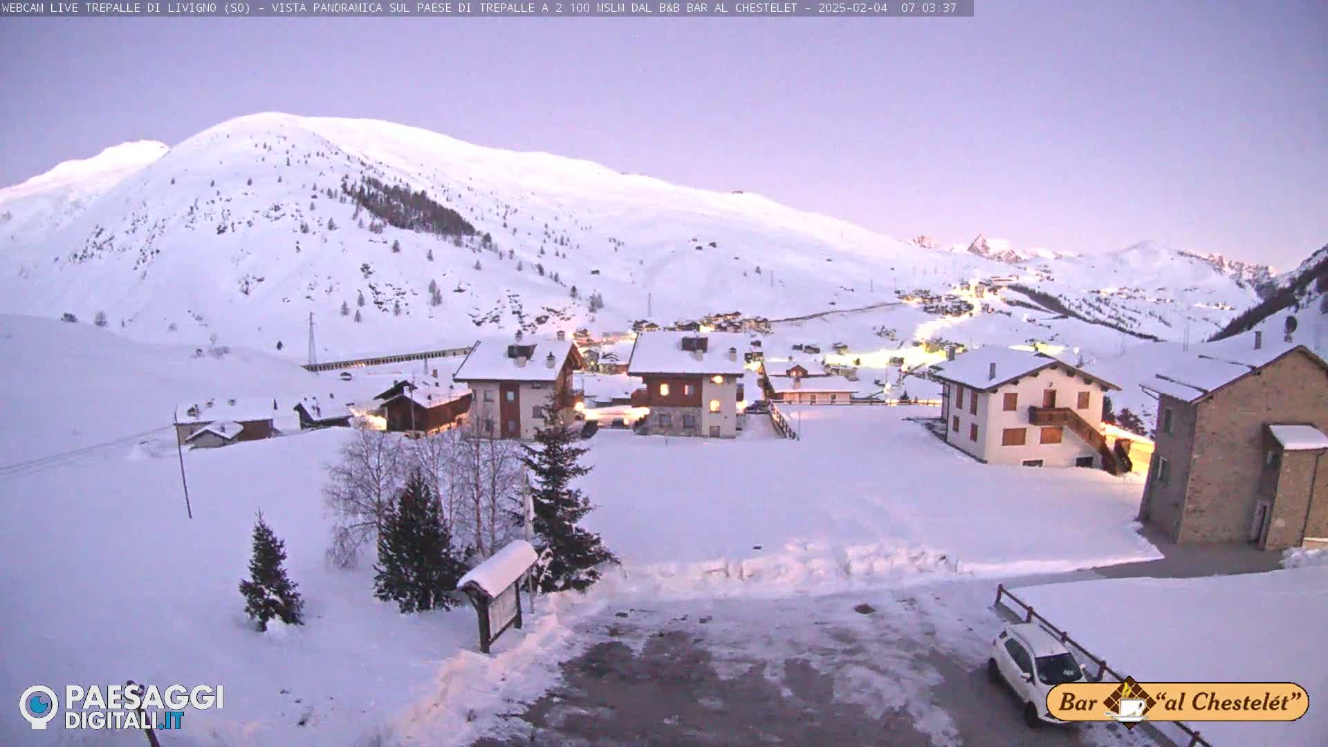 A snow-covered village nestled in a valley, surrounded by snow-capped mountains under a twilight sky.