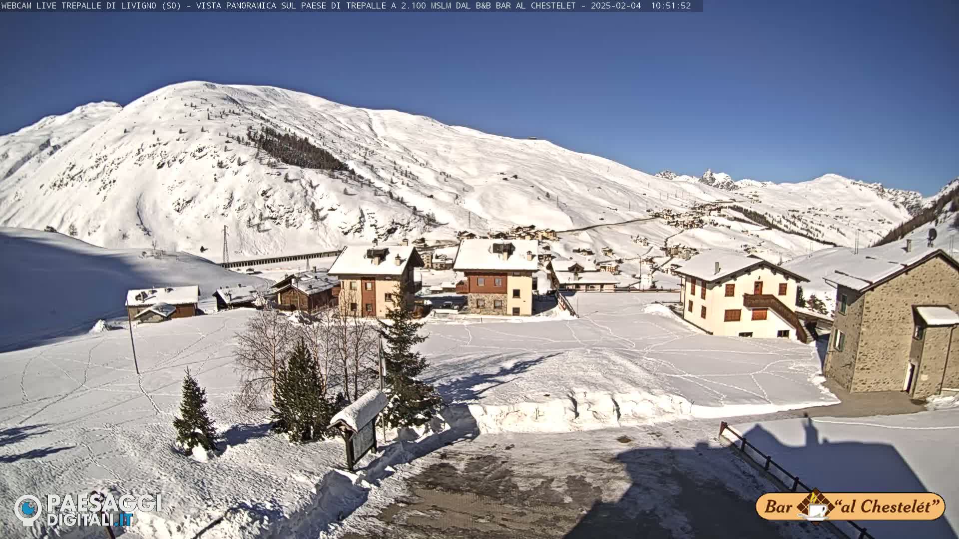 A snow-covered village nestled in a valley between snow-covered mountains under a clear blue sky.