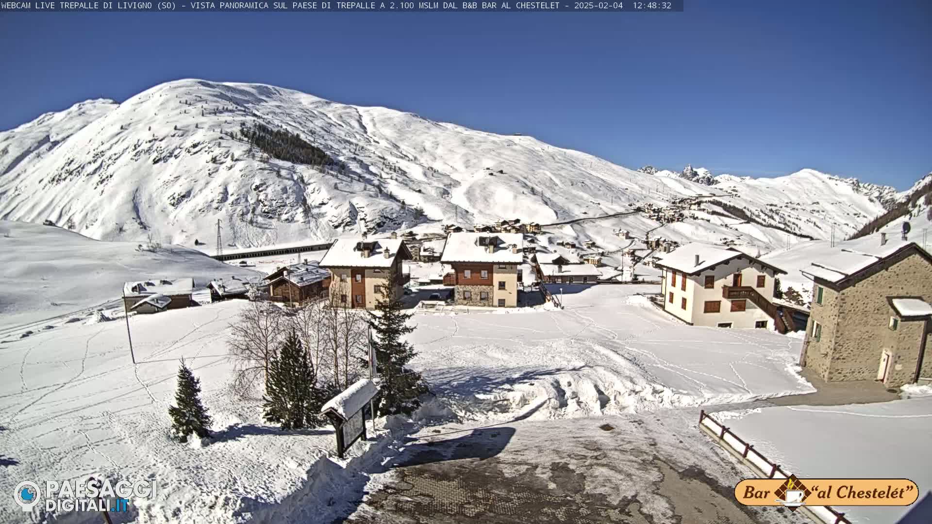 A snow-covered village nestled in a valley surrounded by snow-capped mountains under a clear, sunny sky.