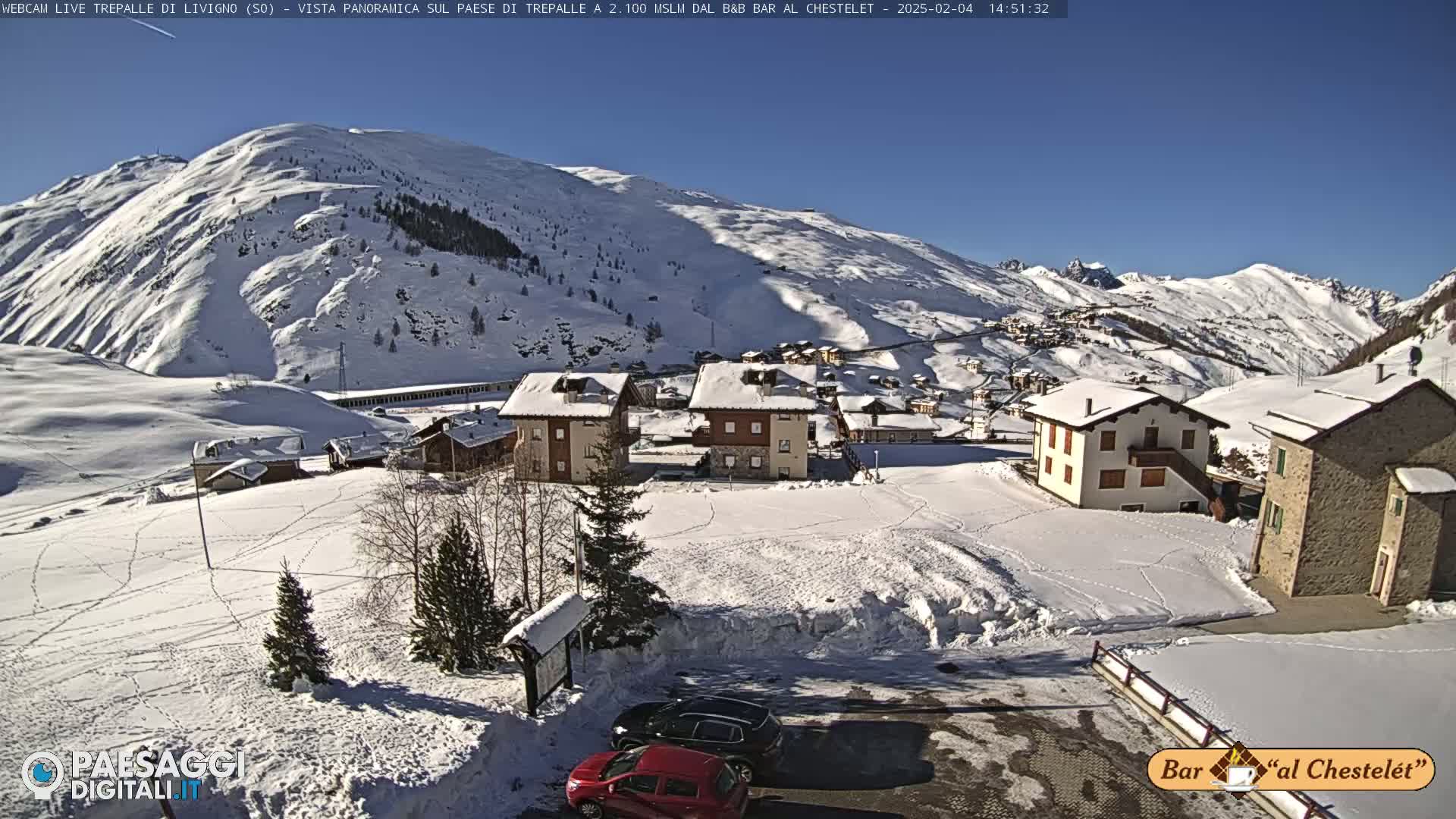 A snow-covered village nestled in a valley, surrounded by snow-capped mountains under a clear blue sky.