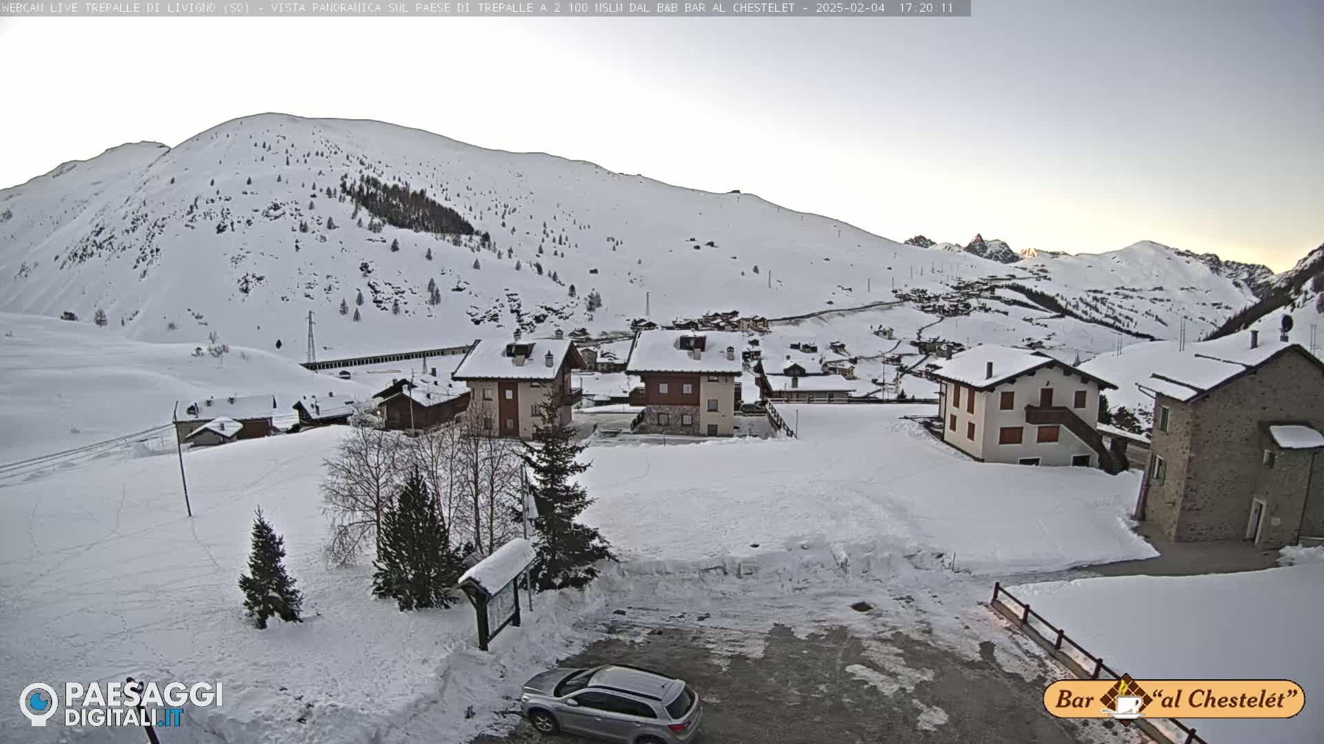 A snow-covered village nestled in a valley beneath a snow-dusted mountain range under a clear, twilight sky.