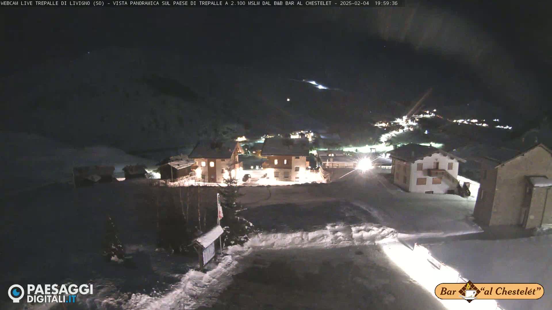 A snow-covered village is illuminated at night, under a dark, clear sky.