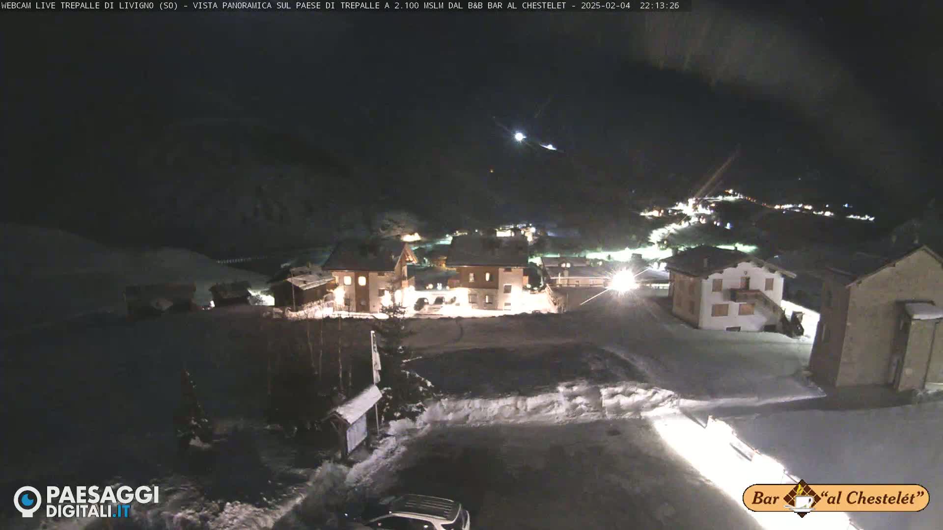 A nighttime, snow-covered village is illuminated, with a clear, dark sky above.