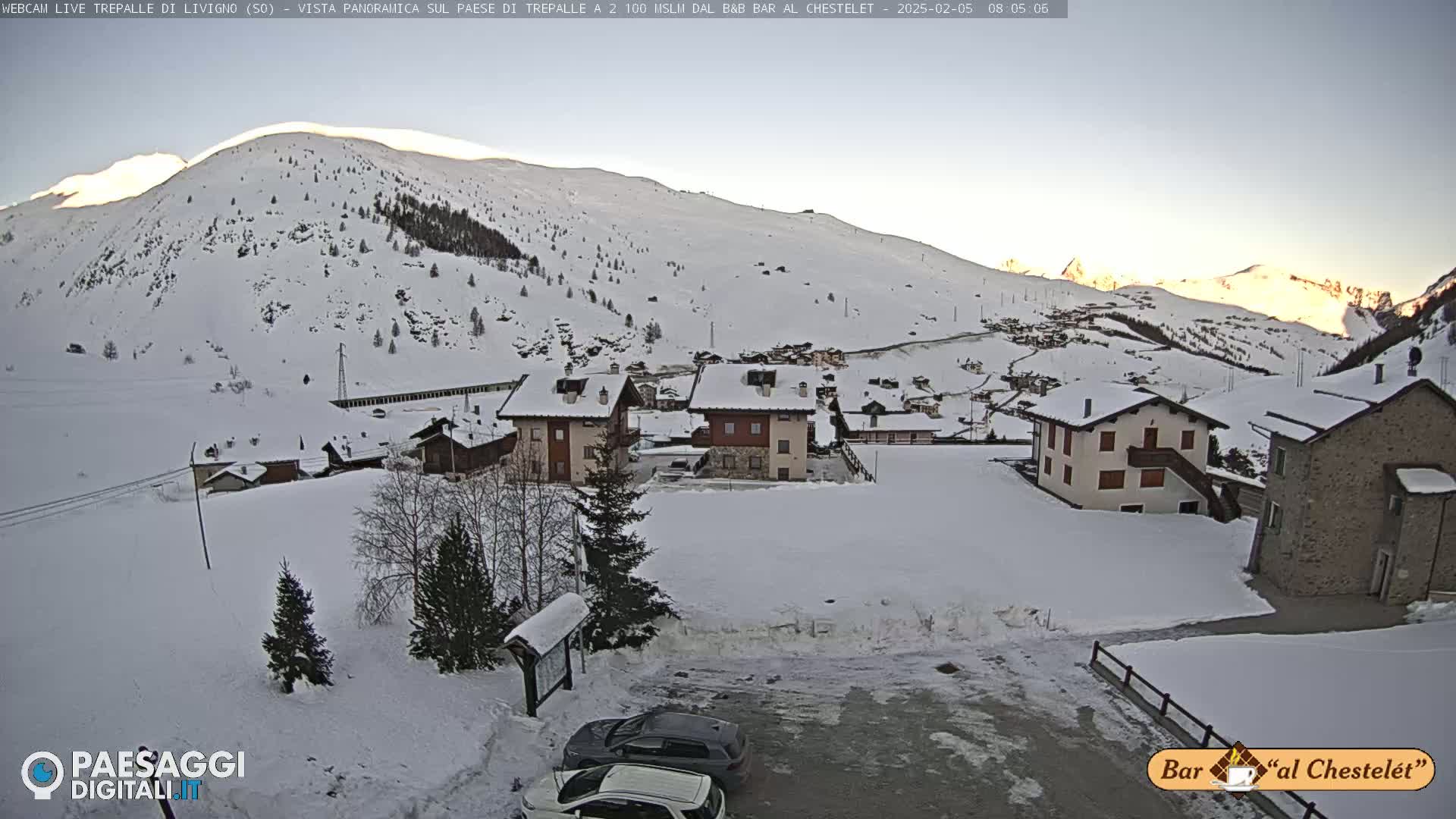A snow-covered village nestled in a valley, surrounded by snow-capped mountains under a clear, bright sky.