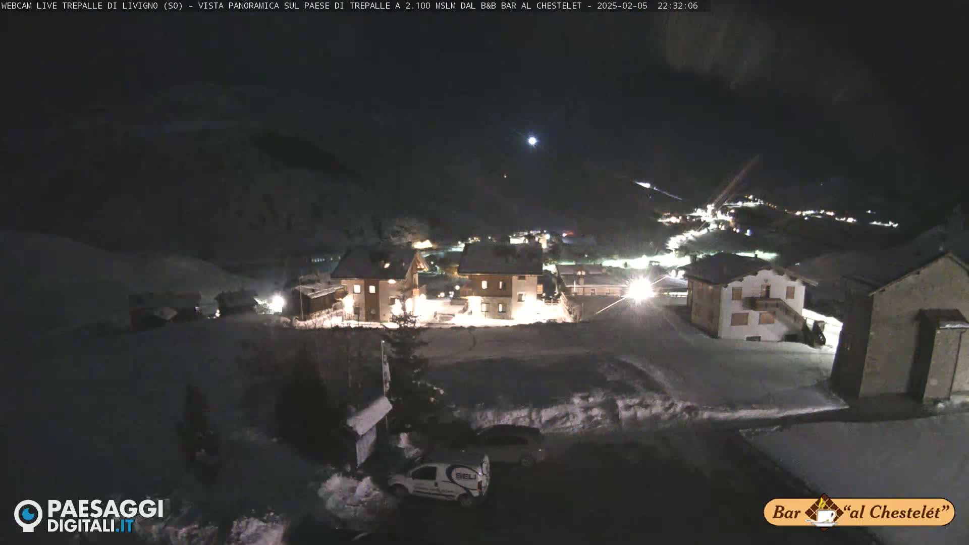 A snow-covered village is illuminated at night, under a dark sky.