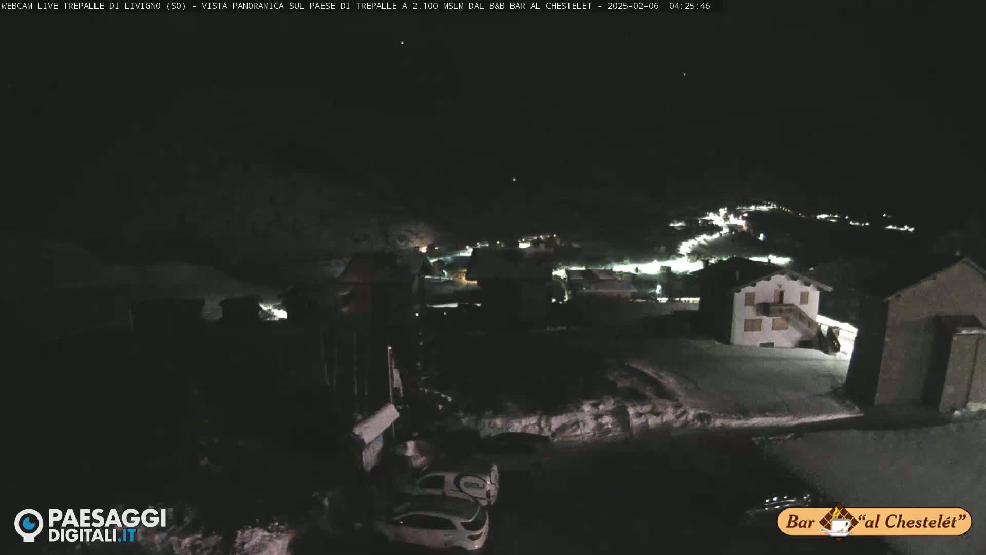 A nighttime, snow-covered village is illuminated by scattered lights under a dark sky.