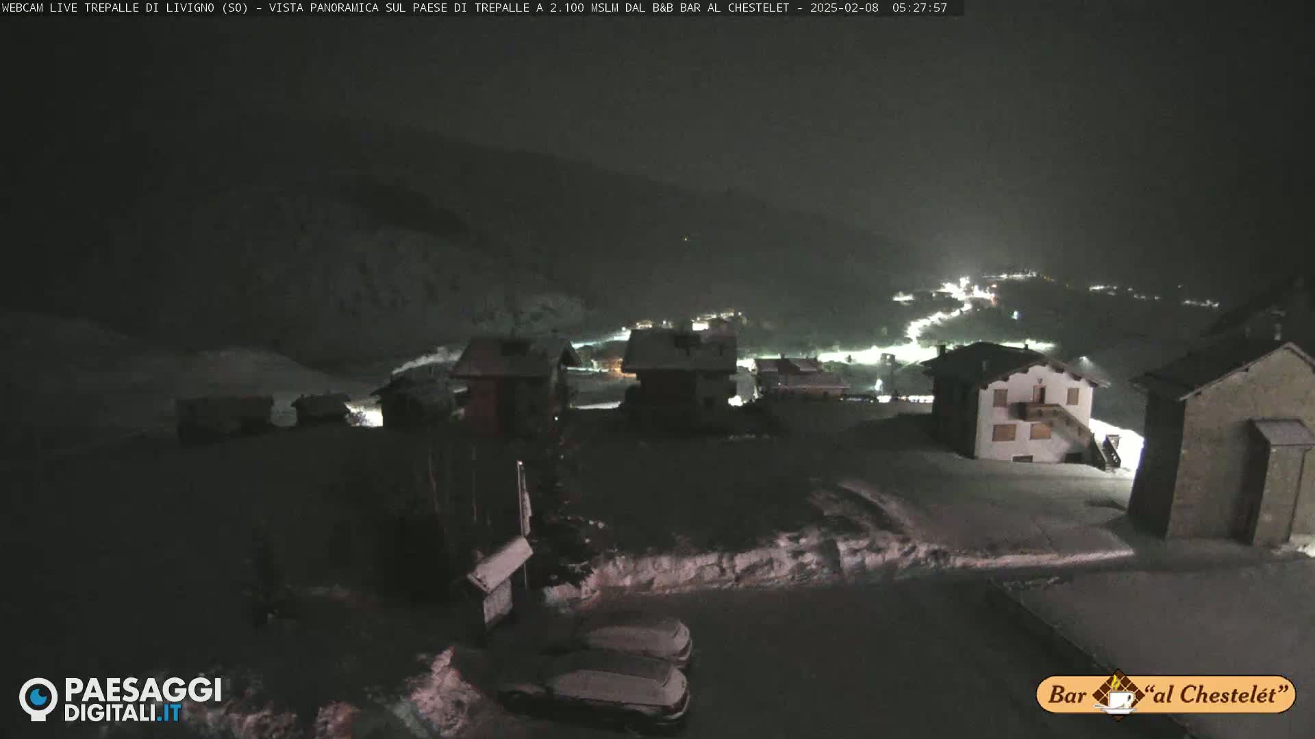 A nighttime, snow-covered village is illuminated by scattered lights under a dark sky.