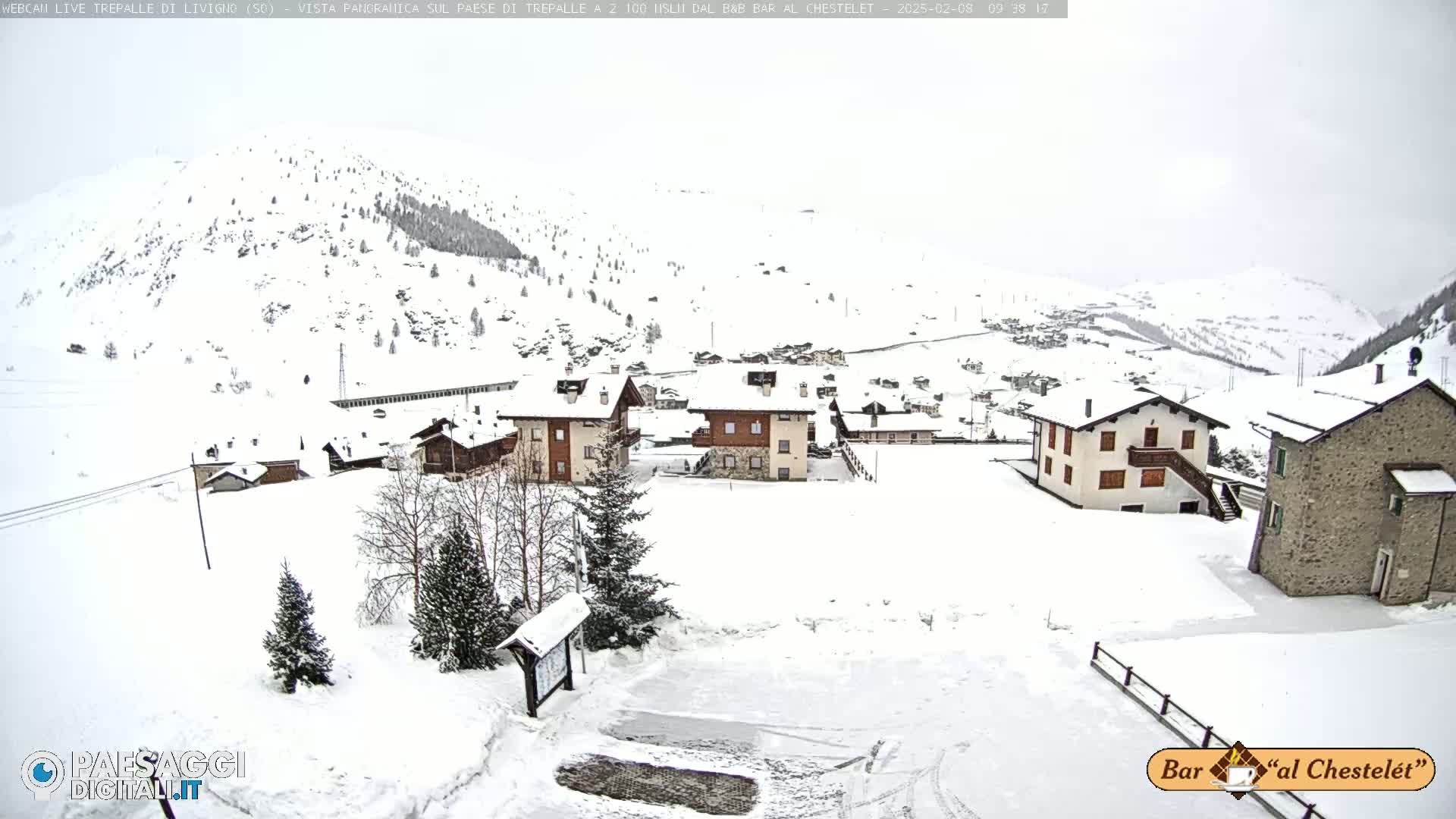 A snow-covered village nestled in a valley between snow-covered mountains on an overcast day.