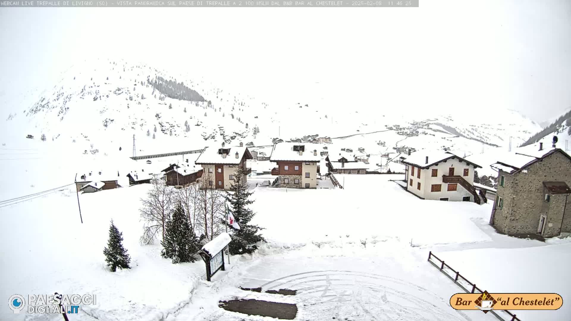 A snow-covered village nestled in a valley among snow-covered mountains under an overcast sky.