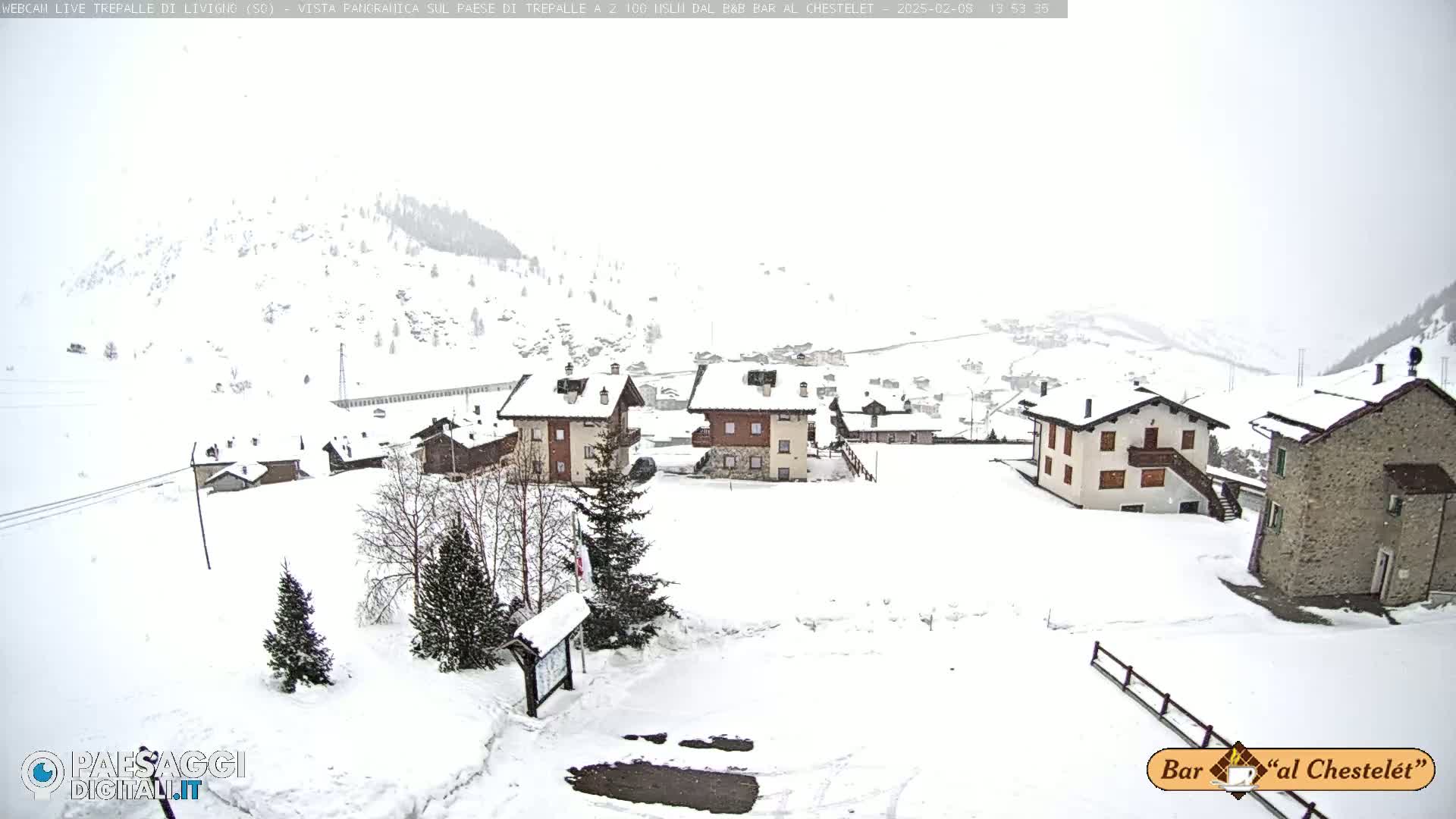 A snow-covered village nestled in a mountainous region during a light snowfall.