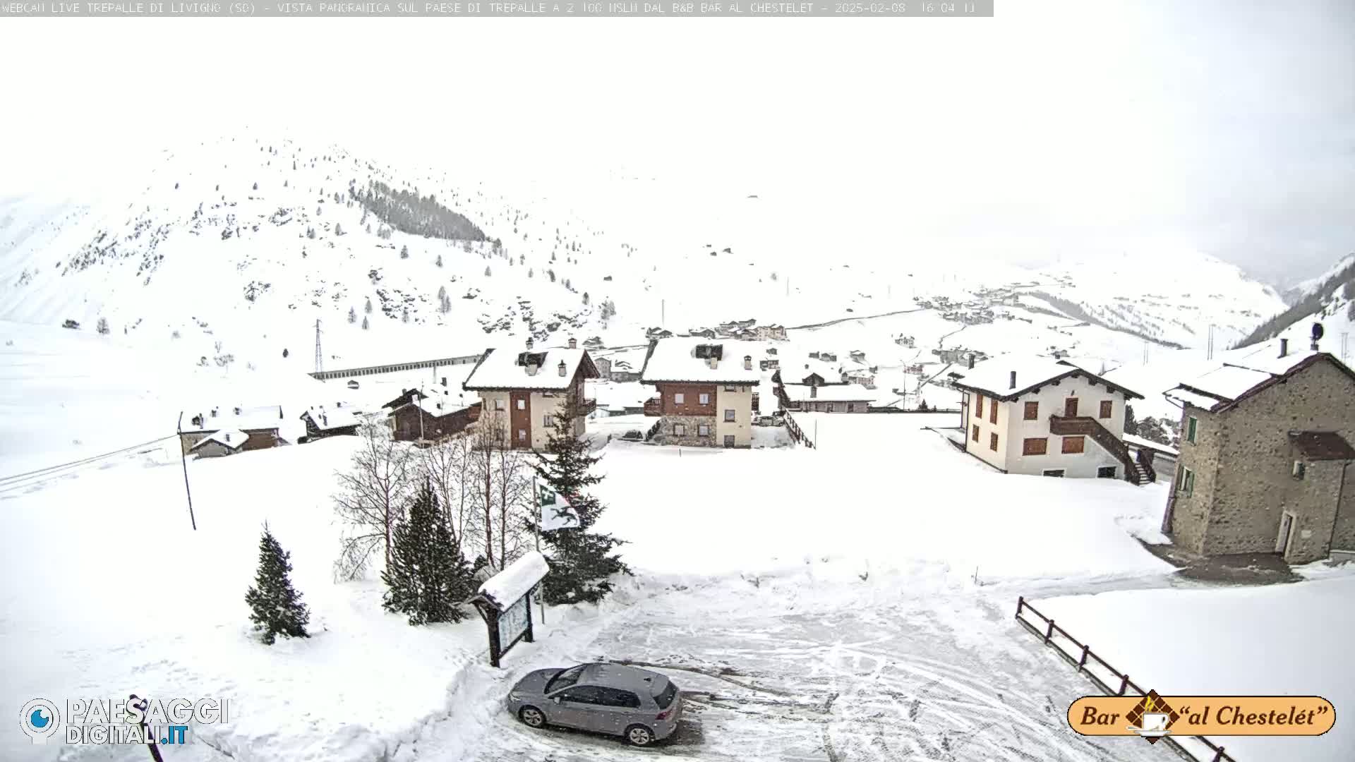 A snow-covered village nestled in a mountainous region, with a car parked in a snow-covered lot in the foreground.