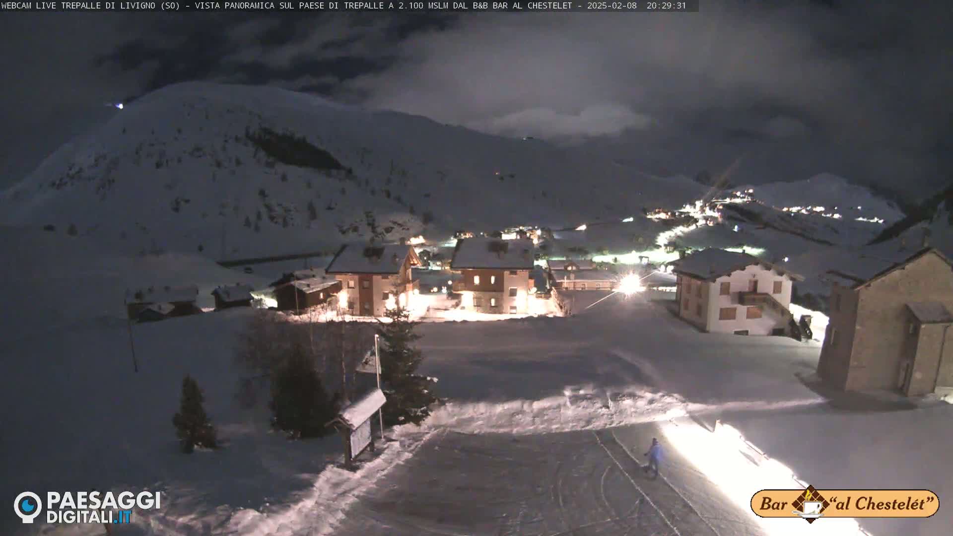 A snow-covered village is illuminated at night under a dark, cloudy sky.