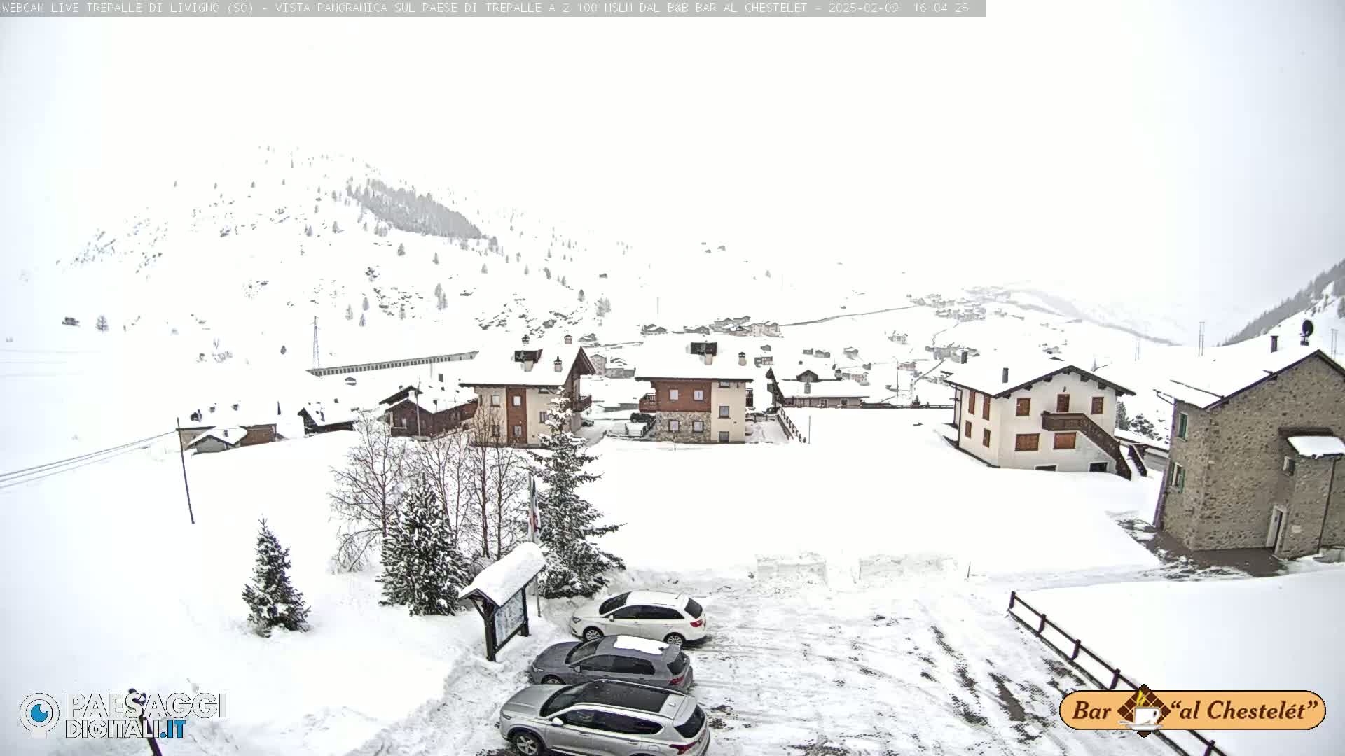 A snow-covered village nestled in a mountainous region during a light snowfall.