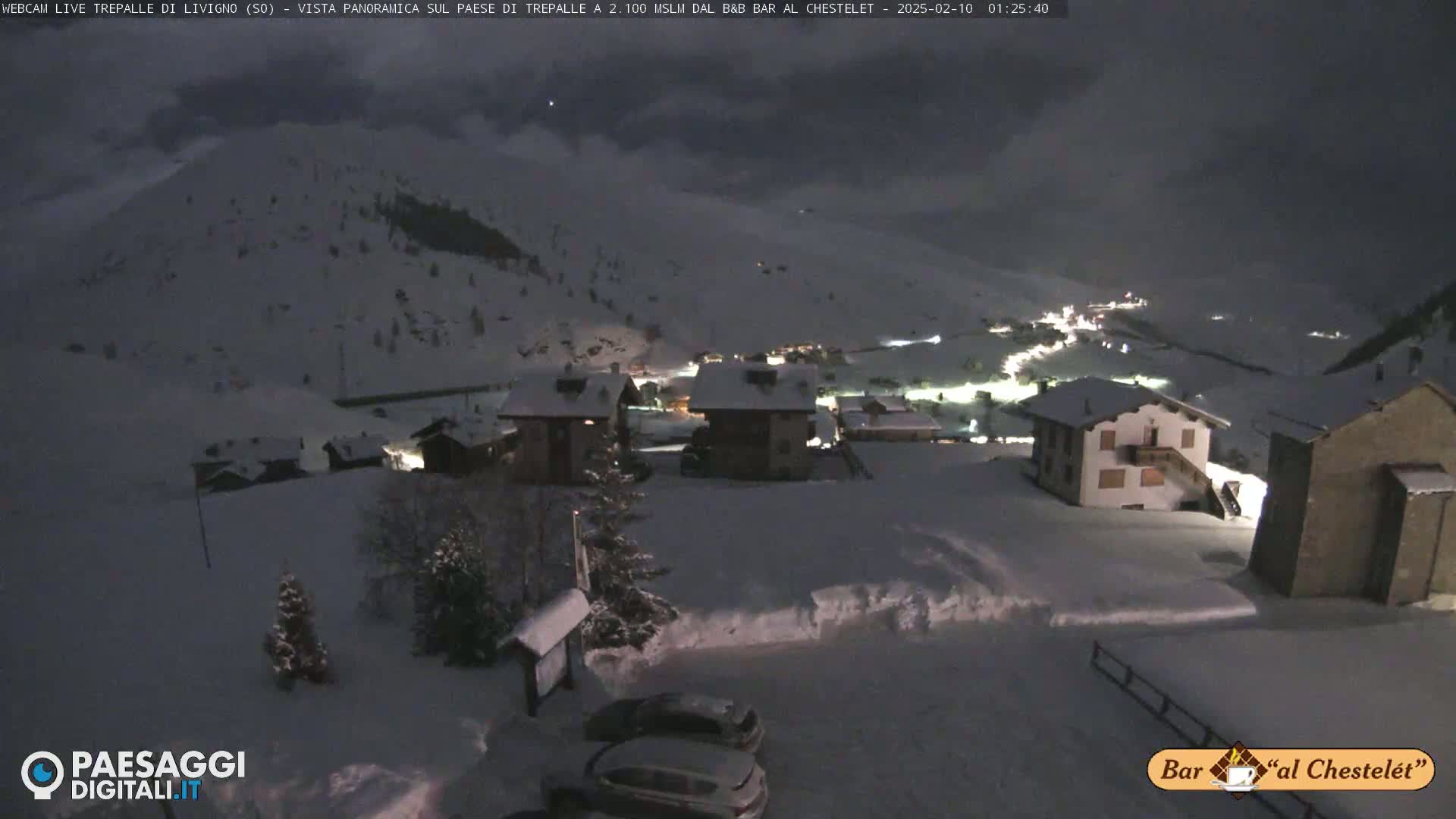 A snow-covered village at night, nestled in a mountainous landscape under a dark, cloudy sky.