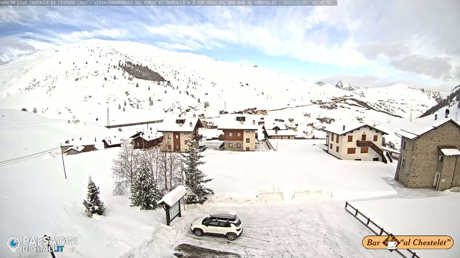 A snow-covered village nestled in a mountainous region under a partly cloudy sky.