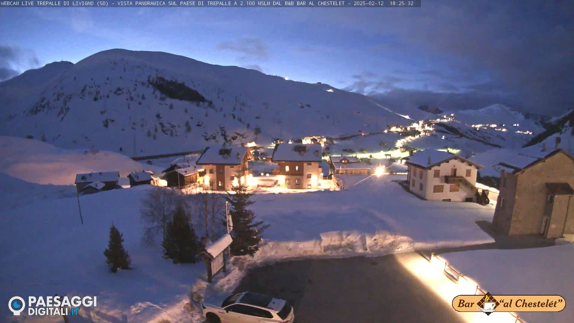 A snow-covered village nestled in a mountain valley at twilight, illuminated by the lights of buildings.