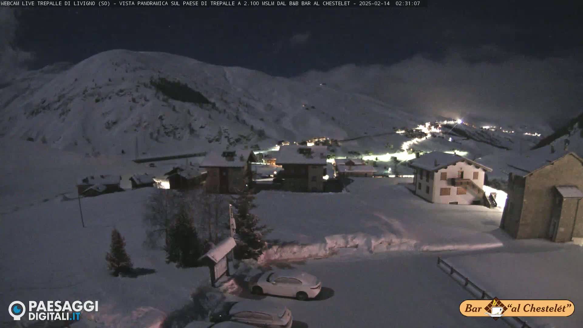 A snow-covered village nestled in a valley under a dark night sky, illuminated by a few lights.