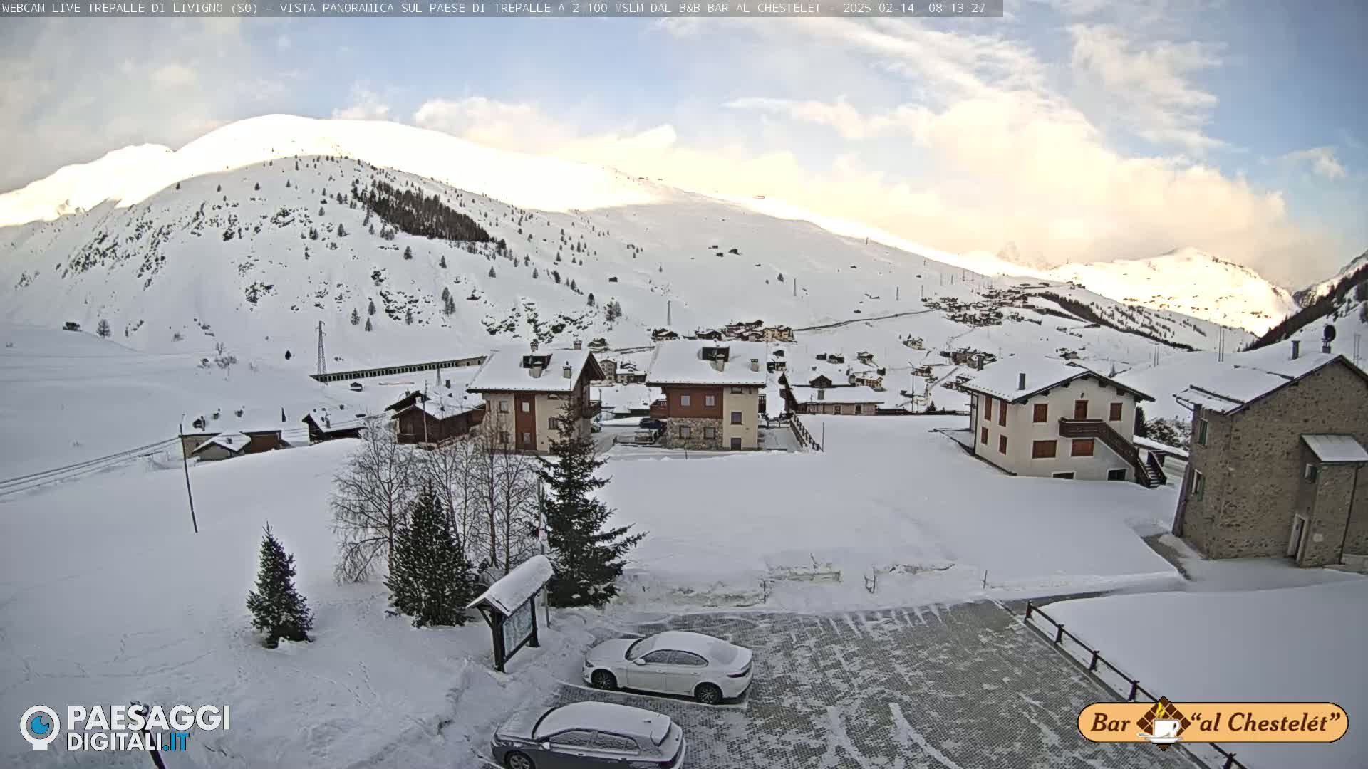 A snow-covered mountain village is seen under a partly cloudy sky.