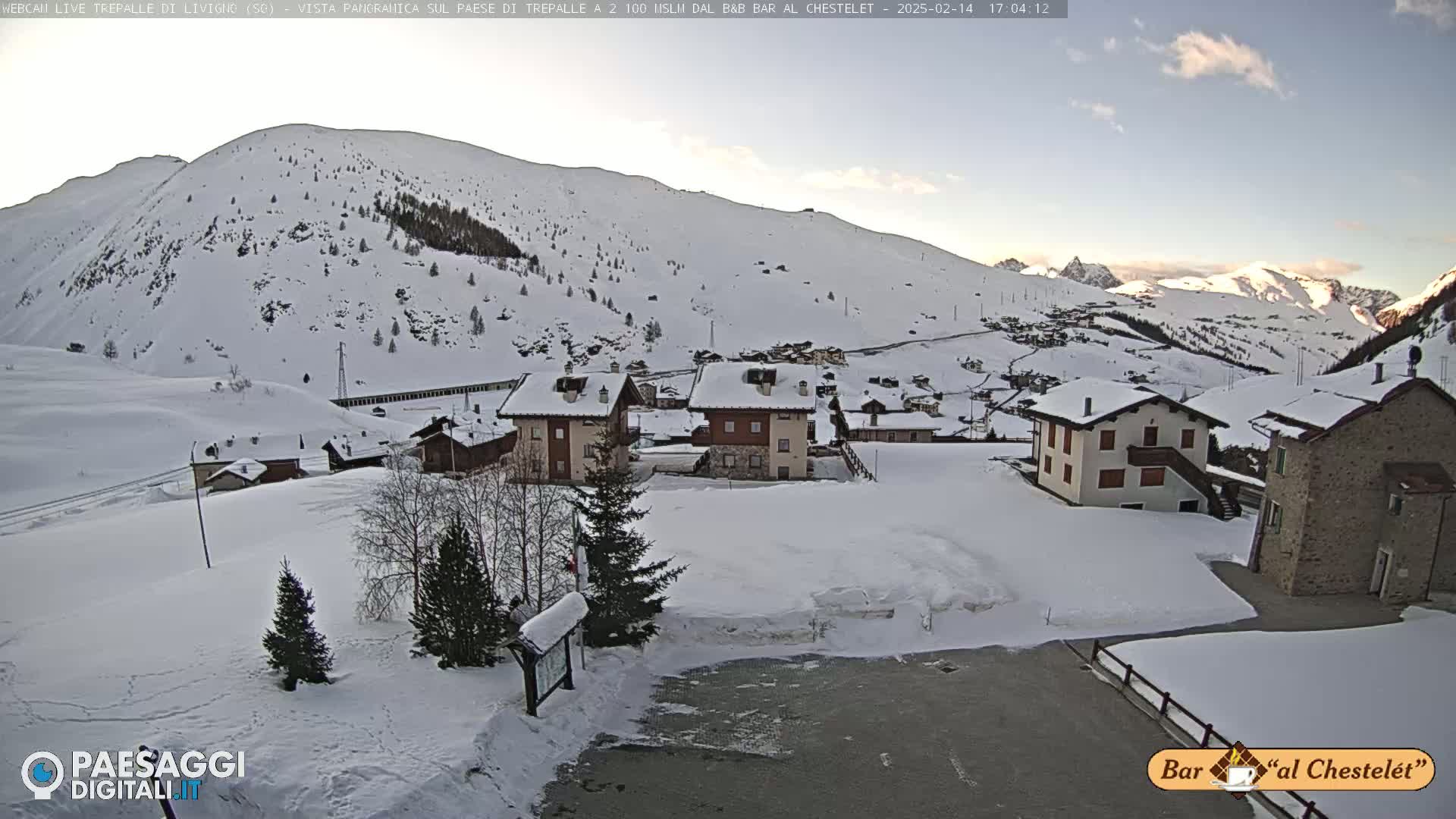 A snow-covered village nestled in a valley, with snow-covered mountains in the background under a clear, bright sky.