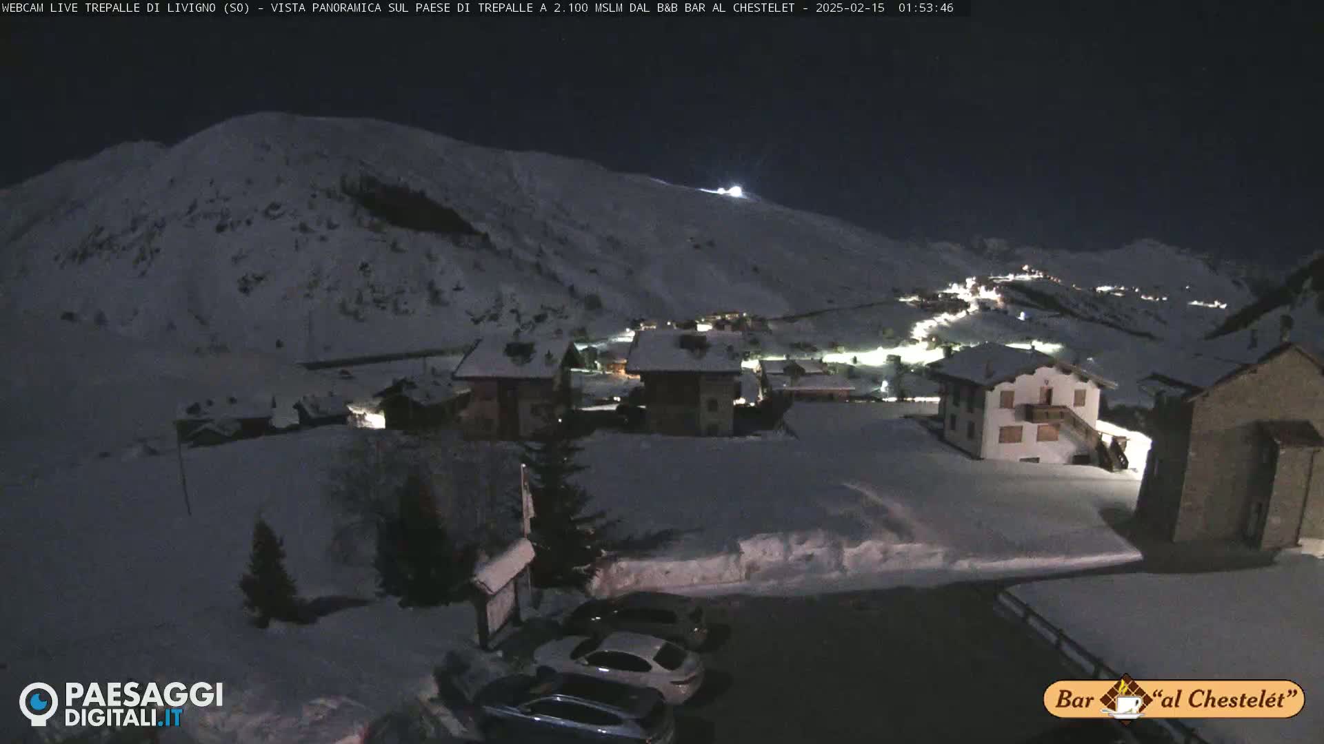 A snow-covered village at night, nestled in a valley beneath a snow-capped mountain.